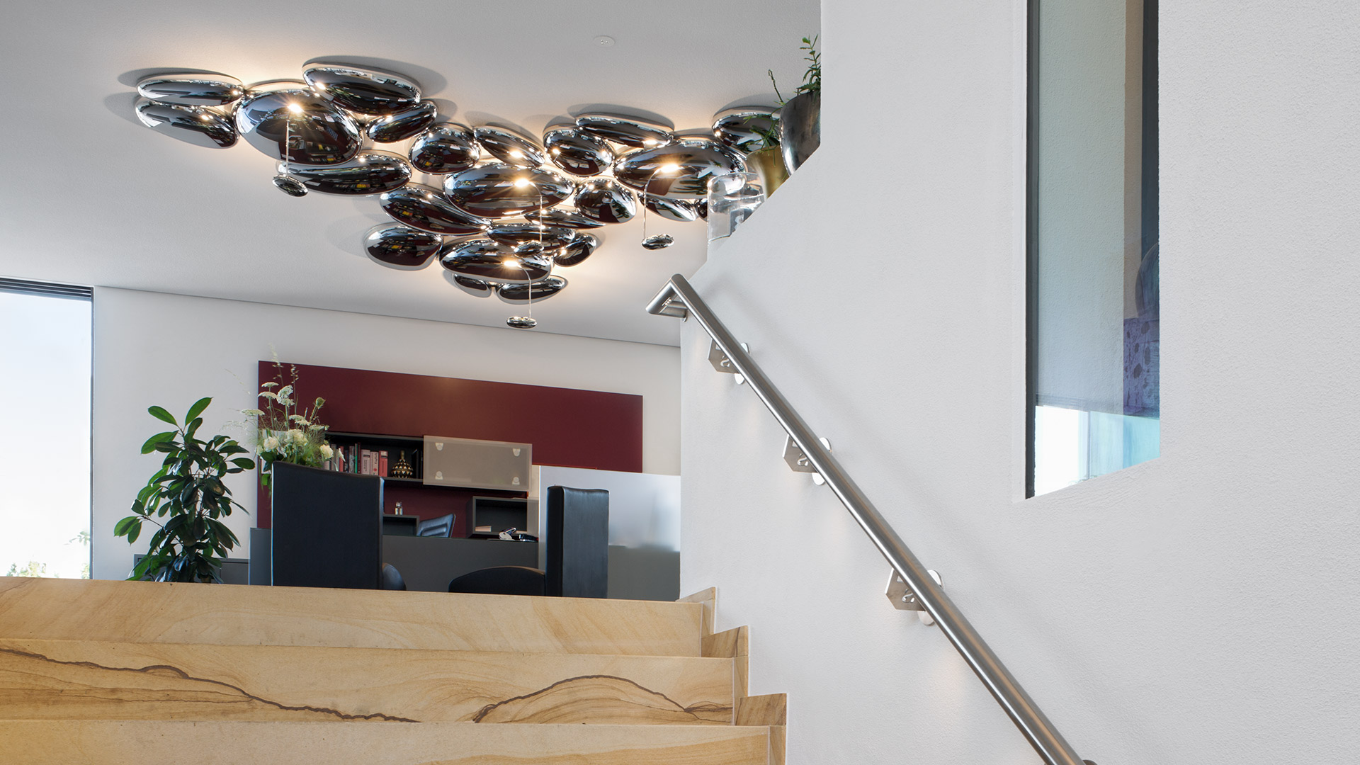 Elegant dining area with dark walls, a snake plant, white chairs, and a chrome bubble-shaped decorative wall sculpture above the table