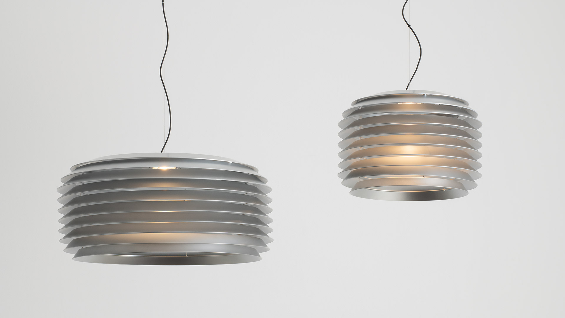 Artemide Slicing pendant lamp with layered grey shade hanging over a round orange side table with decorative objects.