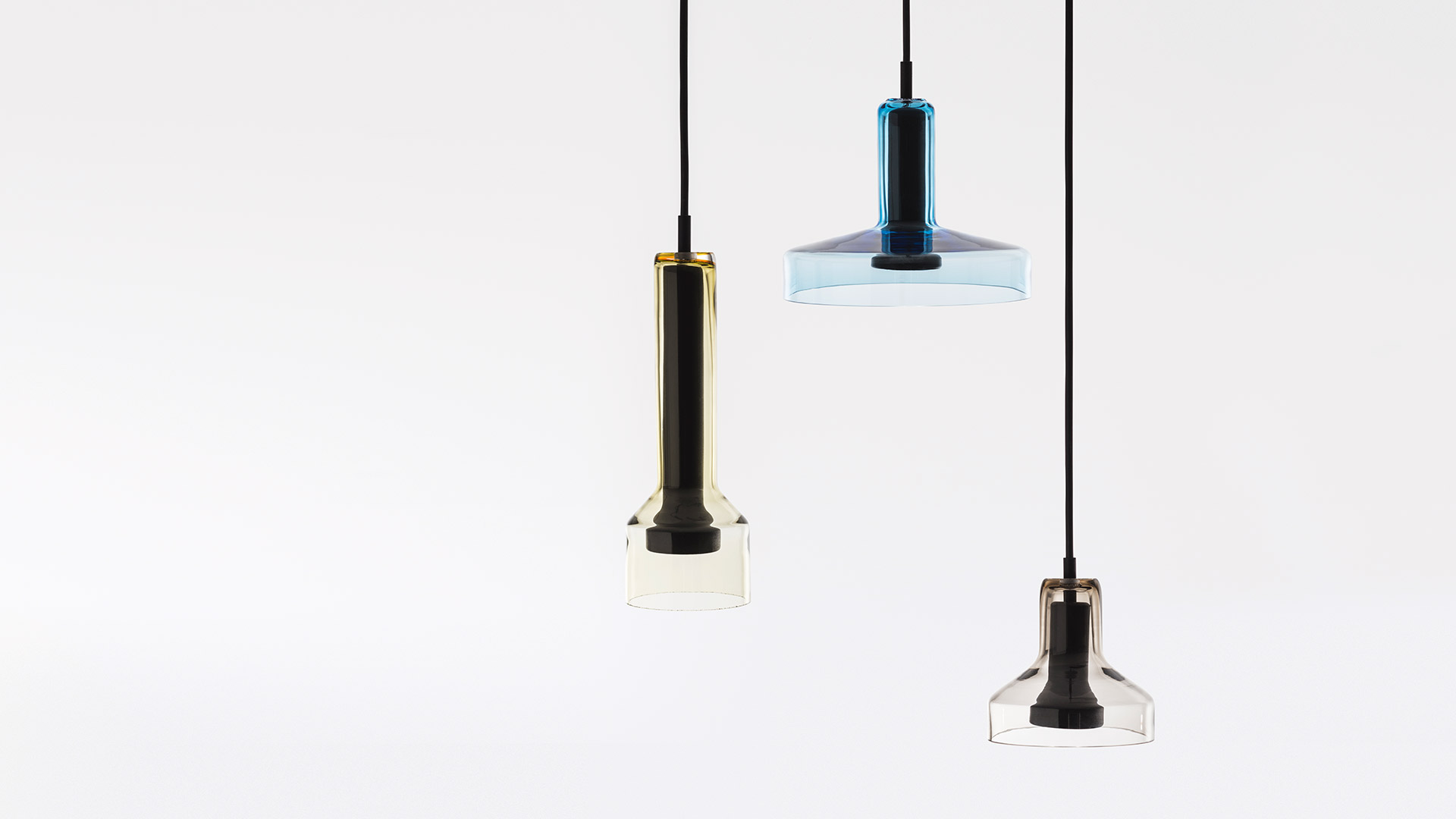 Three Artemide Stablight pendant lamps with blue glass shades hanging at varying heights from a black ceiling canopy on black cords