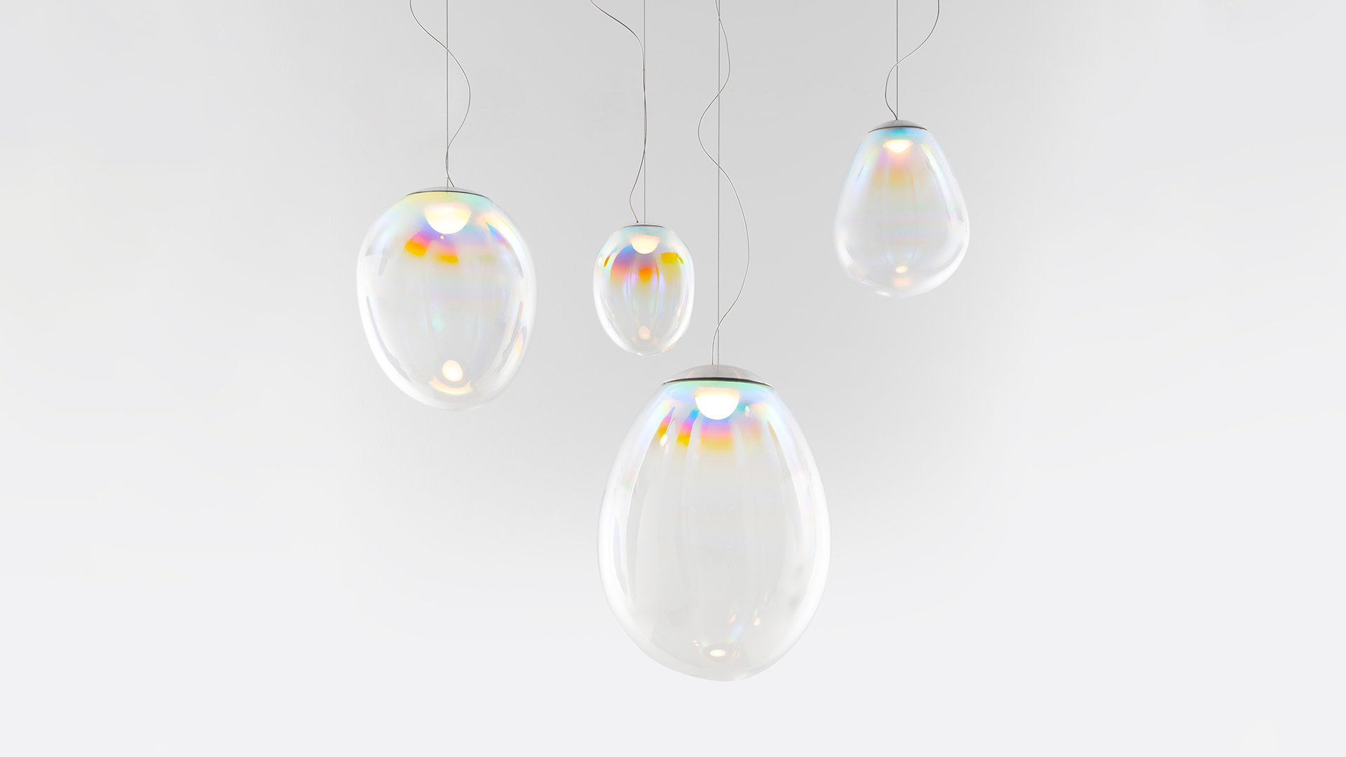 Artemide Stellar Nebula: three iridescent glass pendant lights with rainbow hues, suspended at varying heights from a circular ceiling canopy
