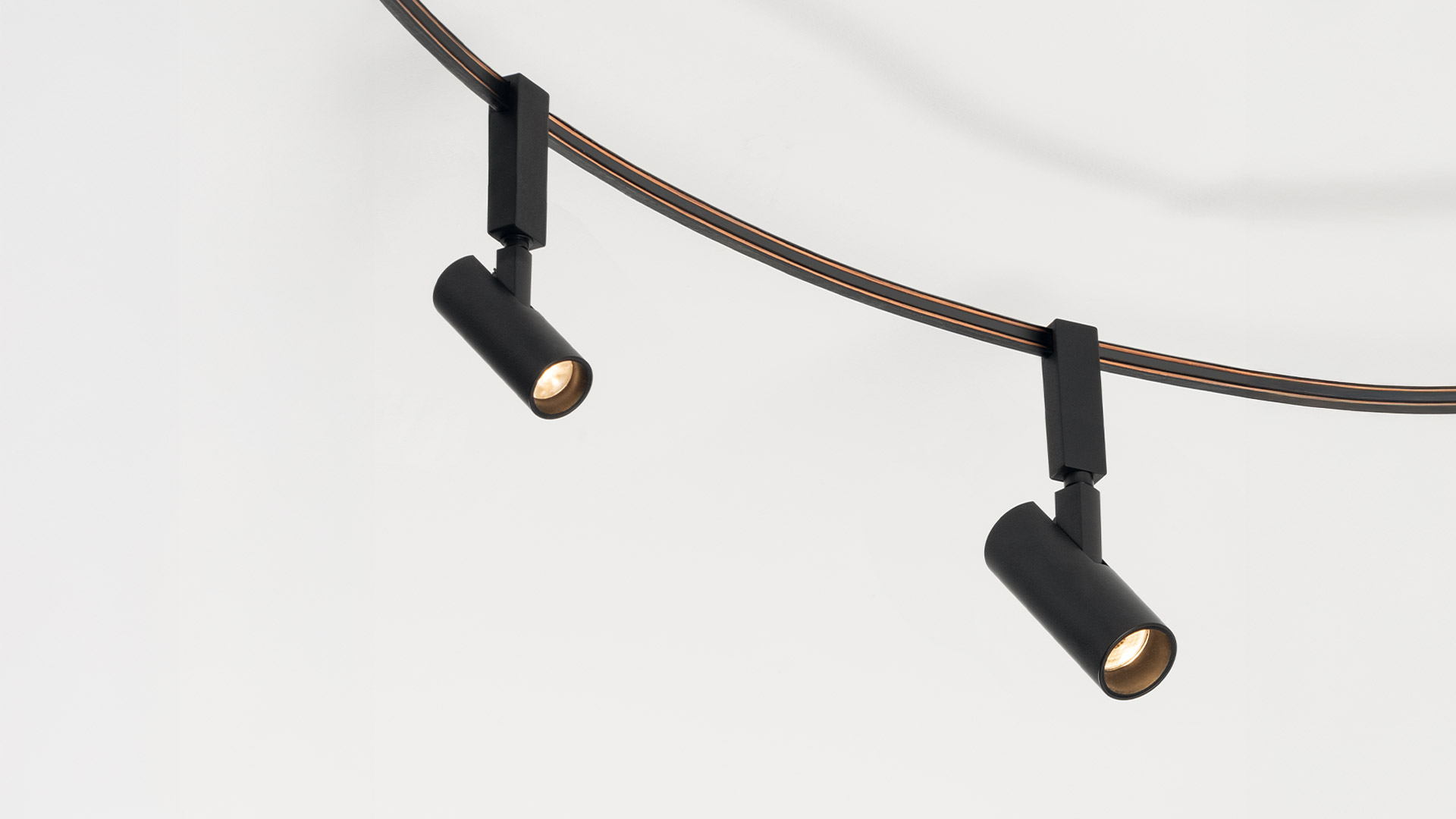 Two hands bending a flexible dark cable into a loop, demonstrating the adjustable structure of the Artemide Sylt lamp