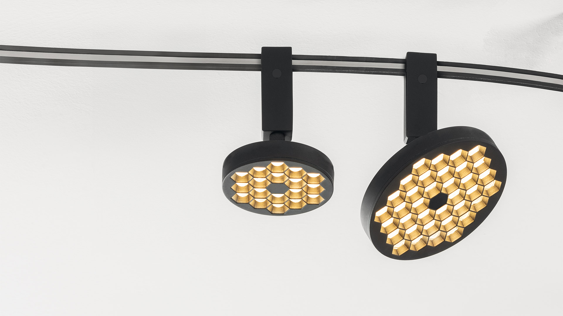 Two Artemide Sylt track spotlights in matte black with gold honeycomb LED arrays, mounted on a curved black rail system
