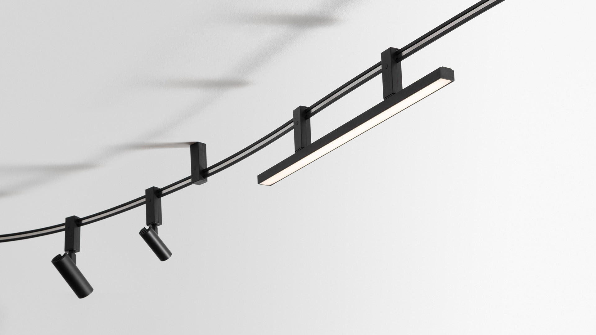 Artemide Sylt ceiling system: two black circular LED spotlights mounted on curved black cables with square ceiling brackets