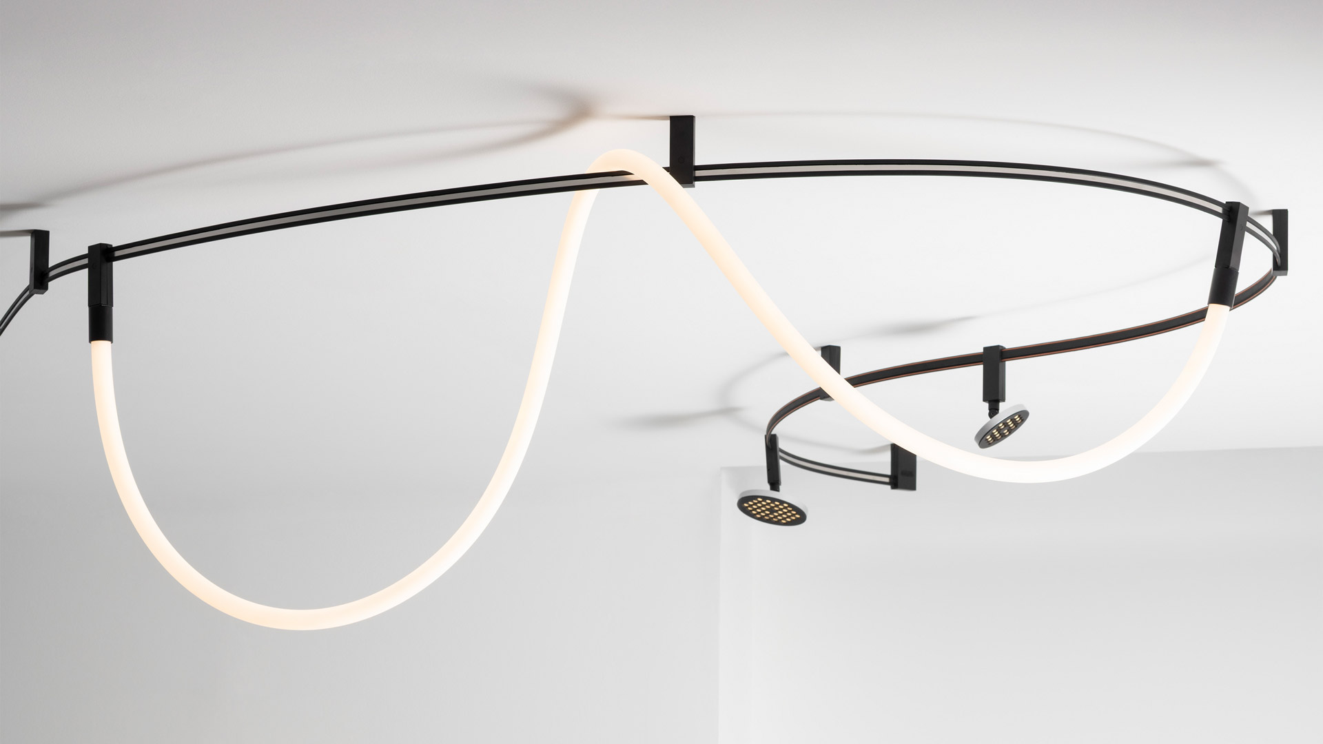 Three Artemide Sylt pendant lamps with opal glass spheres hanging at varying heights from a curved ceiling rail on thin black cords