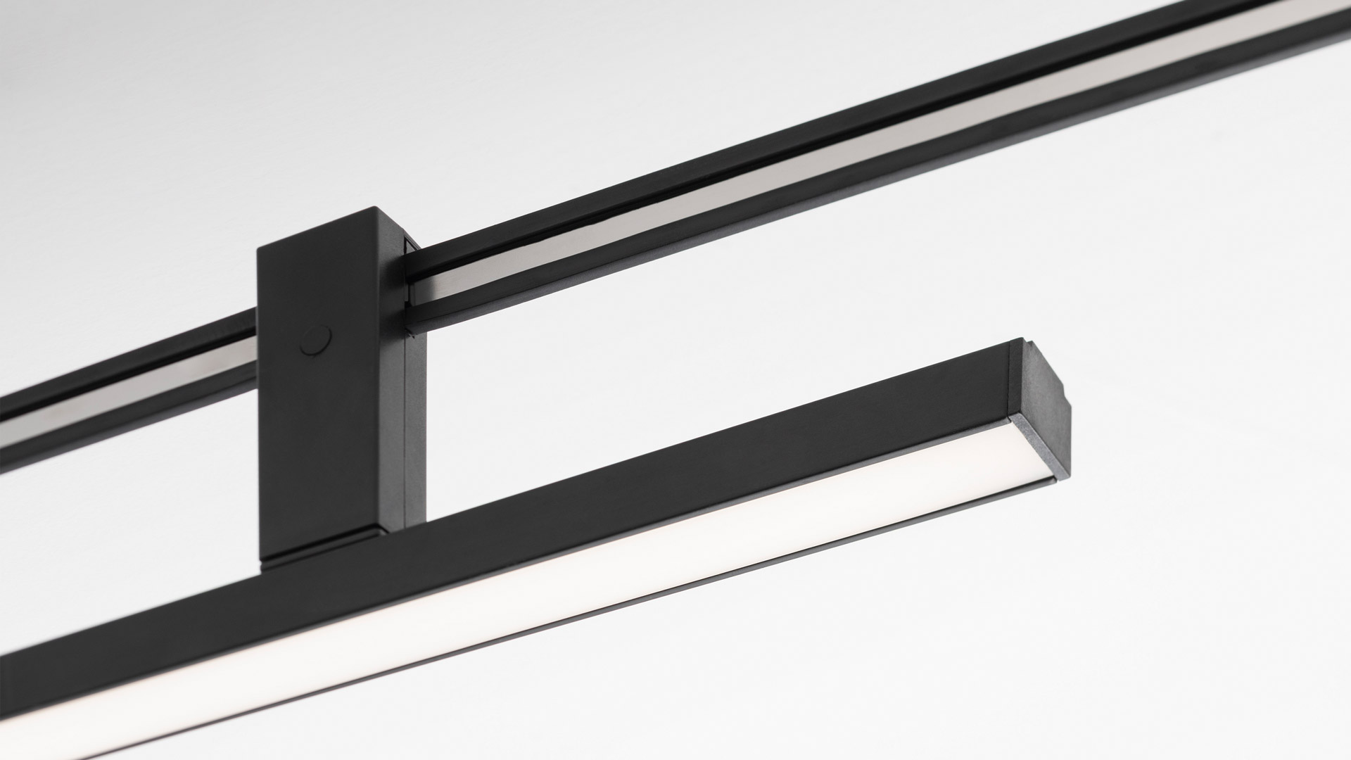 Artemide Sylt system: curved black ceiling track with multiple pendants including cylindrical, spherical glass shades, a brass drop, and a flexible LED tube