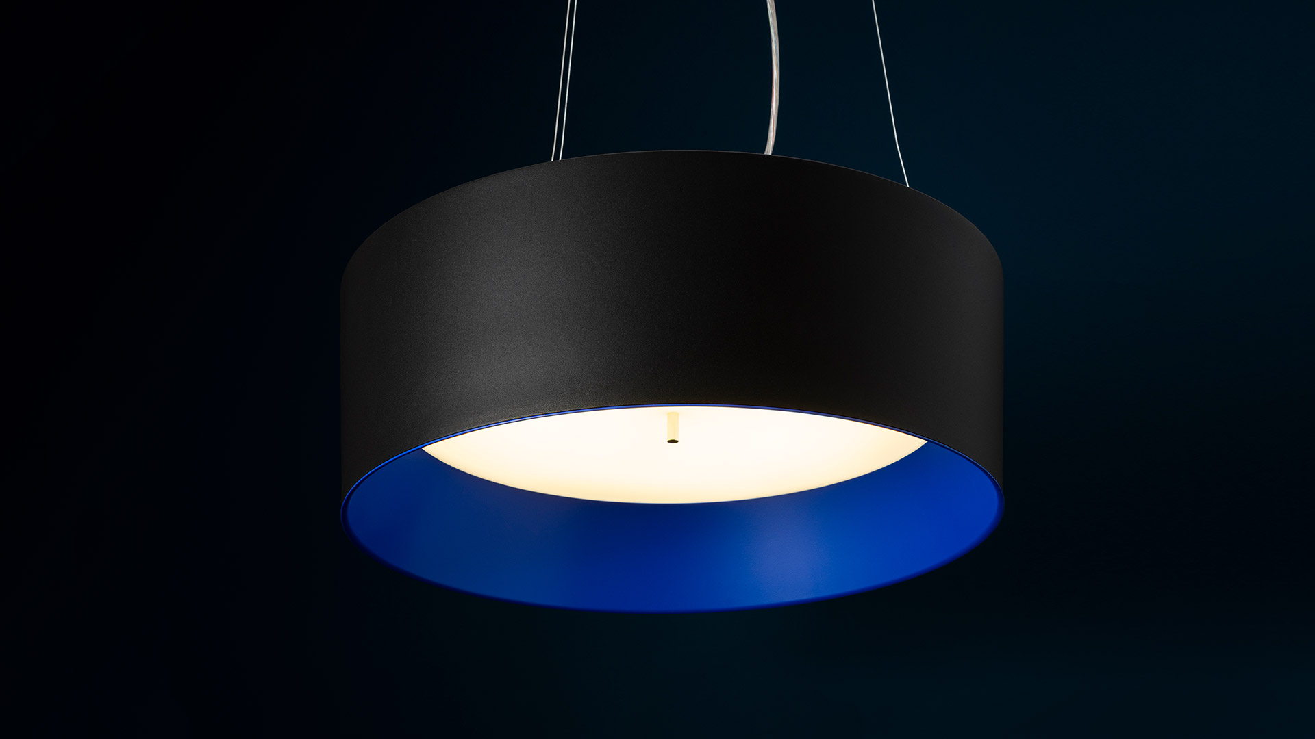 Tagora Sospensione 570 pendant lamp: cylindrical matte black outer shade with vivid blue inner diffuser emitting warm white light