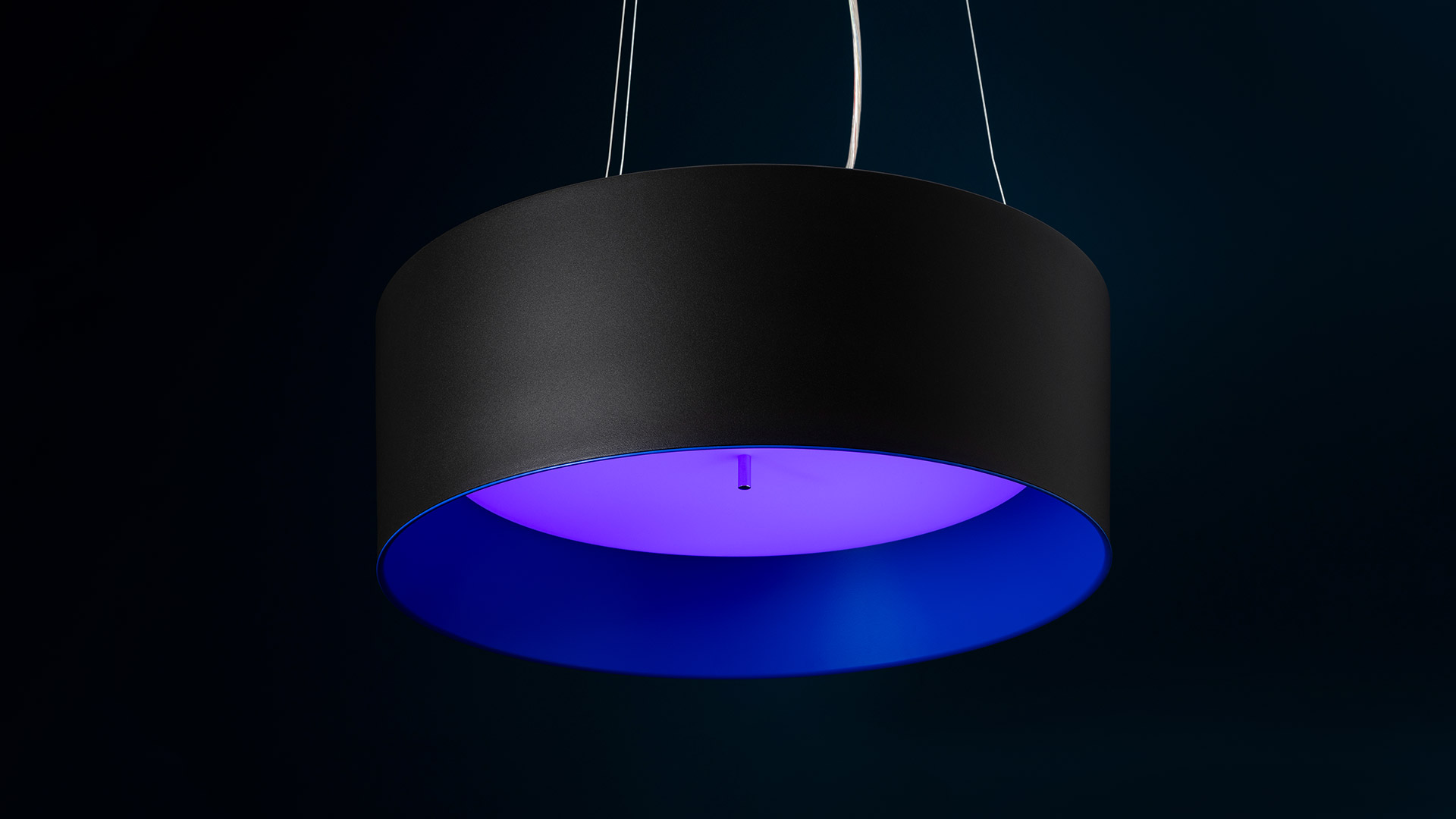 Artemide Tagora Sospensione 570 pendant lamp with matte black cylindrical shade emitting vivid blue-purple light from interior