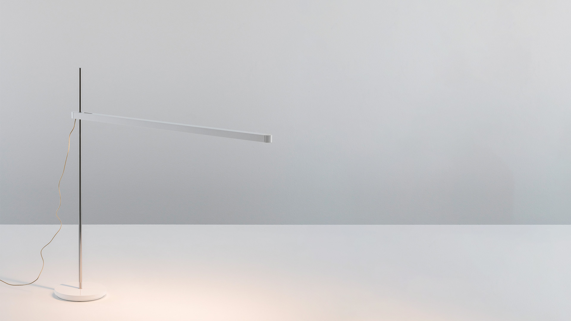 Artemide Talak floor lamp in white, featuring a slender vertical pole and horizontal LED arm, casting warm light on the base