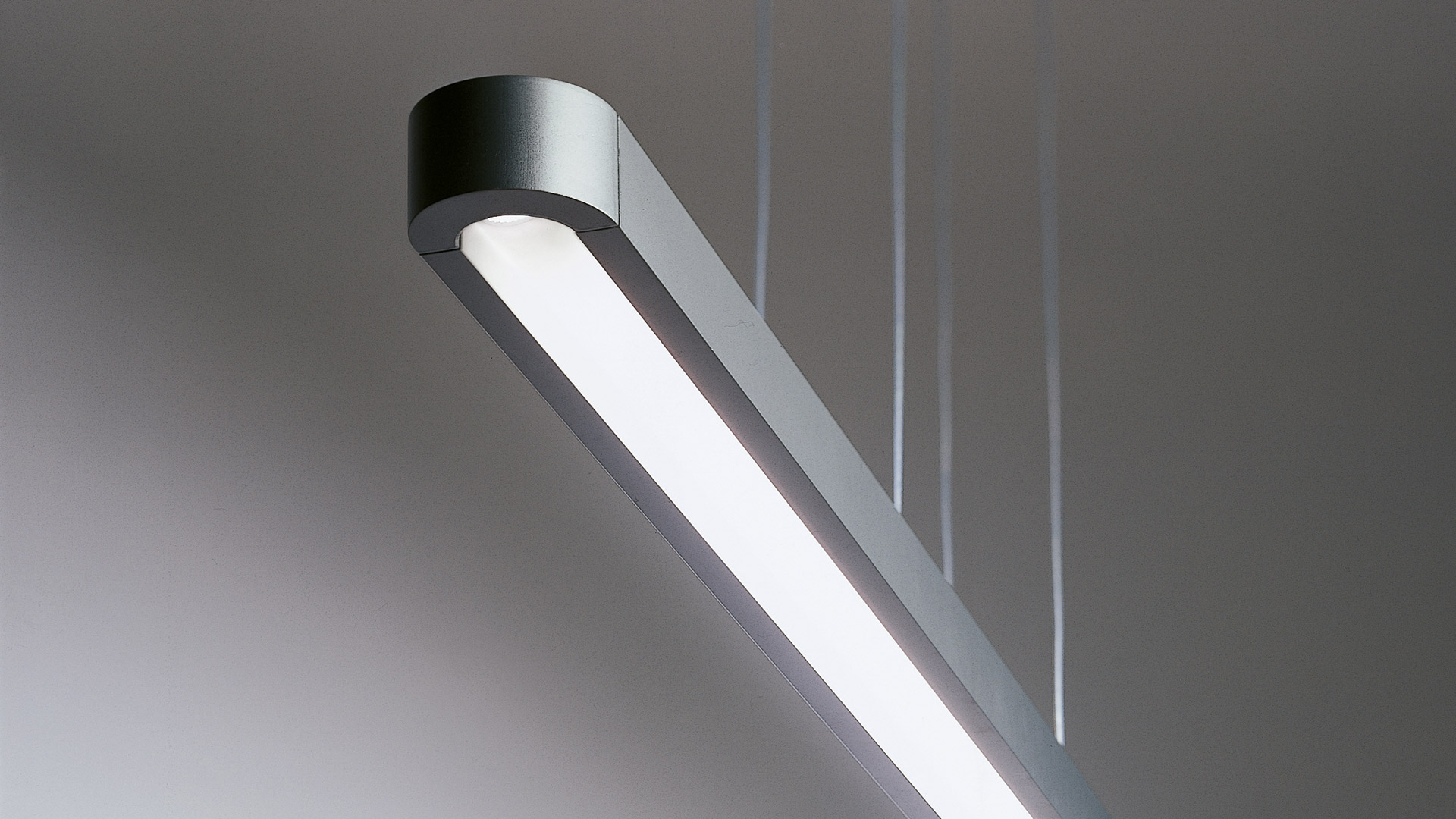 Talo suspension pendant lamp by Artemide: elongated white linear LED fixture with rounded edges, emitting warm light downward