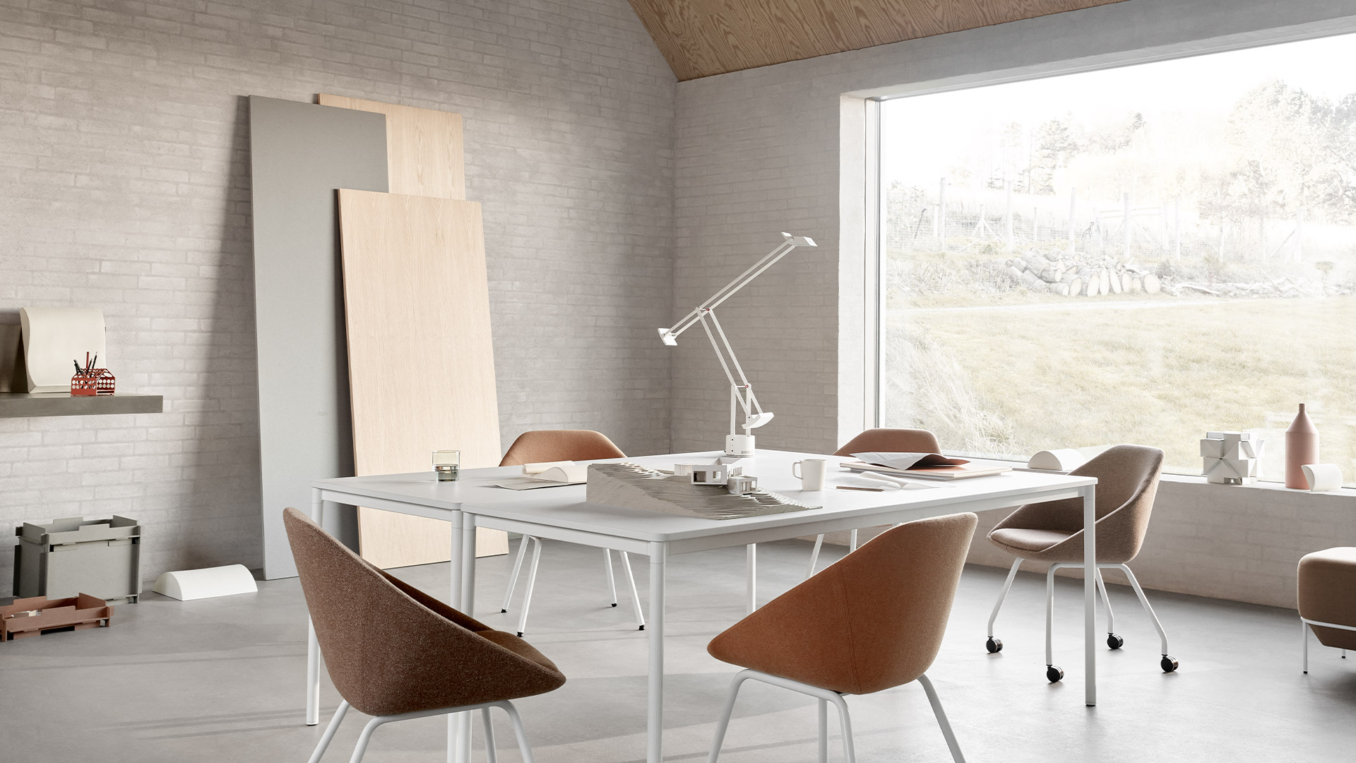 Artemide Tizio black desk lamp with articulated arm on a wooden desk, surrounded by books, pencils, and pinned photos.