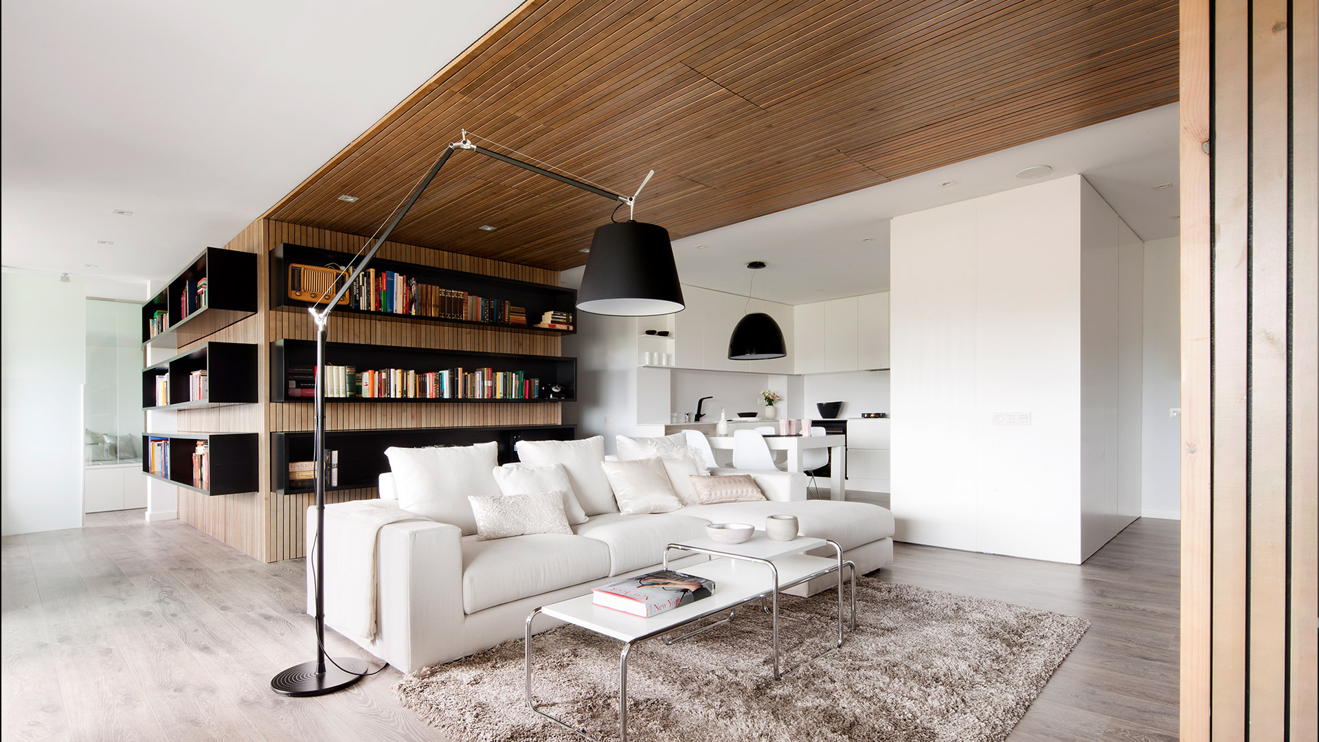 Modern living room with Artemide Tolomeo Mega Terra floor lamp beside a white sofa, wood-paneled ceiling, and built-in bookshelf.