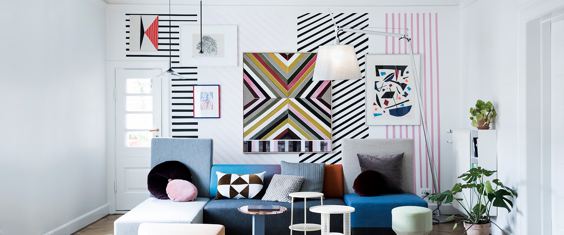 Living room with bold geometric wall art, colorful sectional sofa, and an Artemide Tolomeo Maxi floor lamp with white shade
