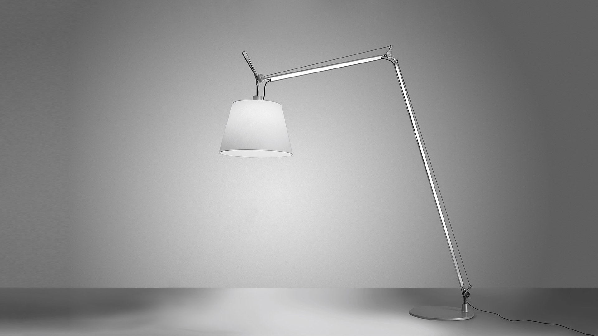 Artemide Tolomeo Maxi floor lamp with articulated aluminum arm and large white conical shade, casting warm light on neutral background