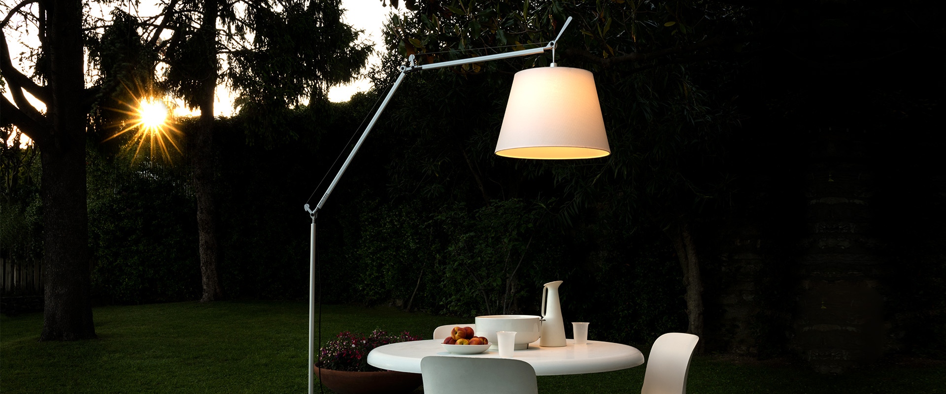 Artemide Tolomeo Paralume Outdoor floor lamp with white shade illuminating a dining table in a garden at dusk
