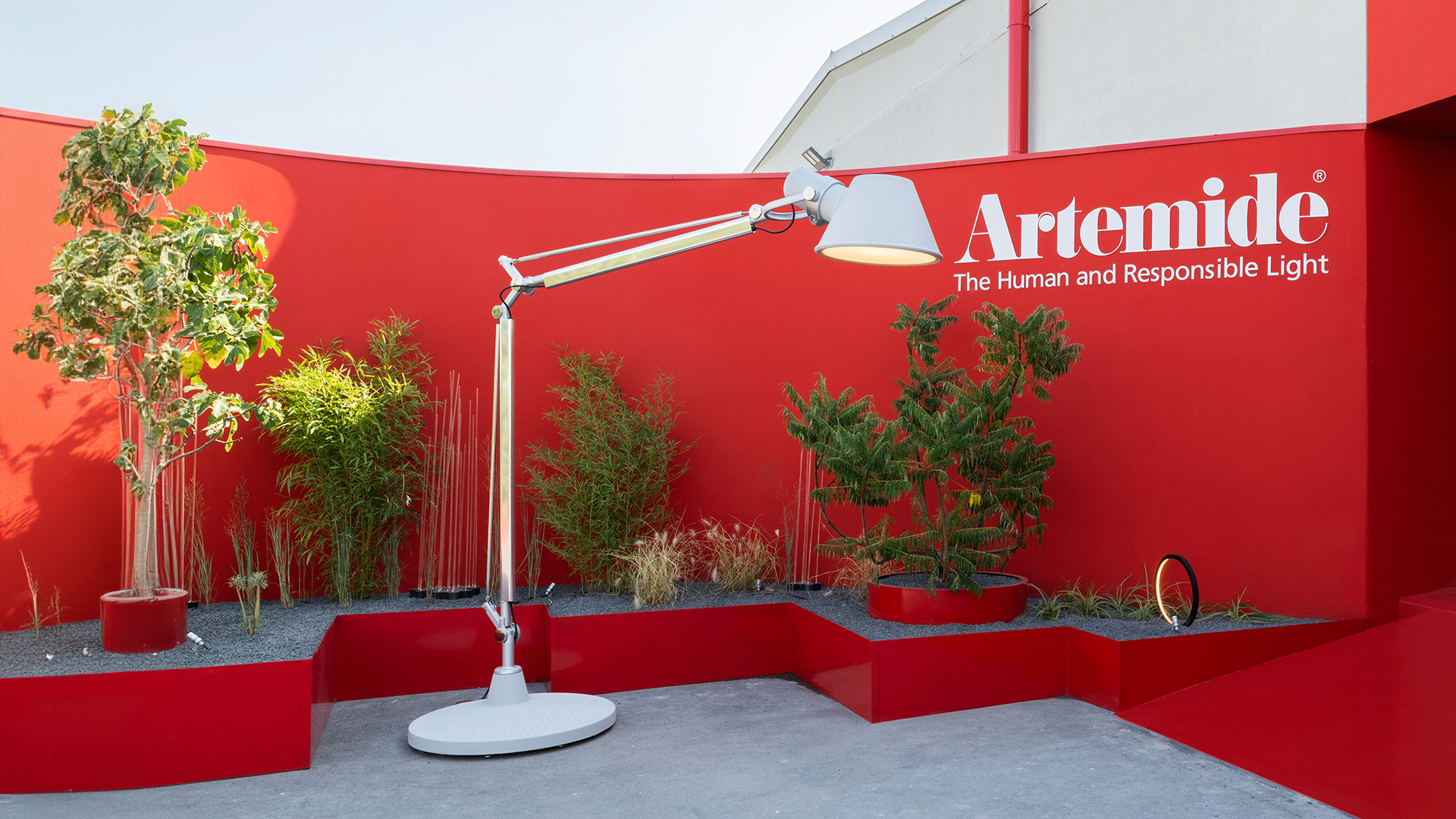Artemide Tolomeo XXL Outdoor floor lamp on a modern wooden deck at dusk, with white modular seating and glass-walled pavilion