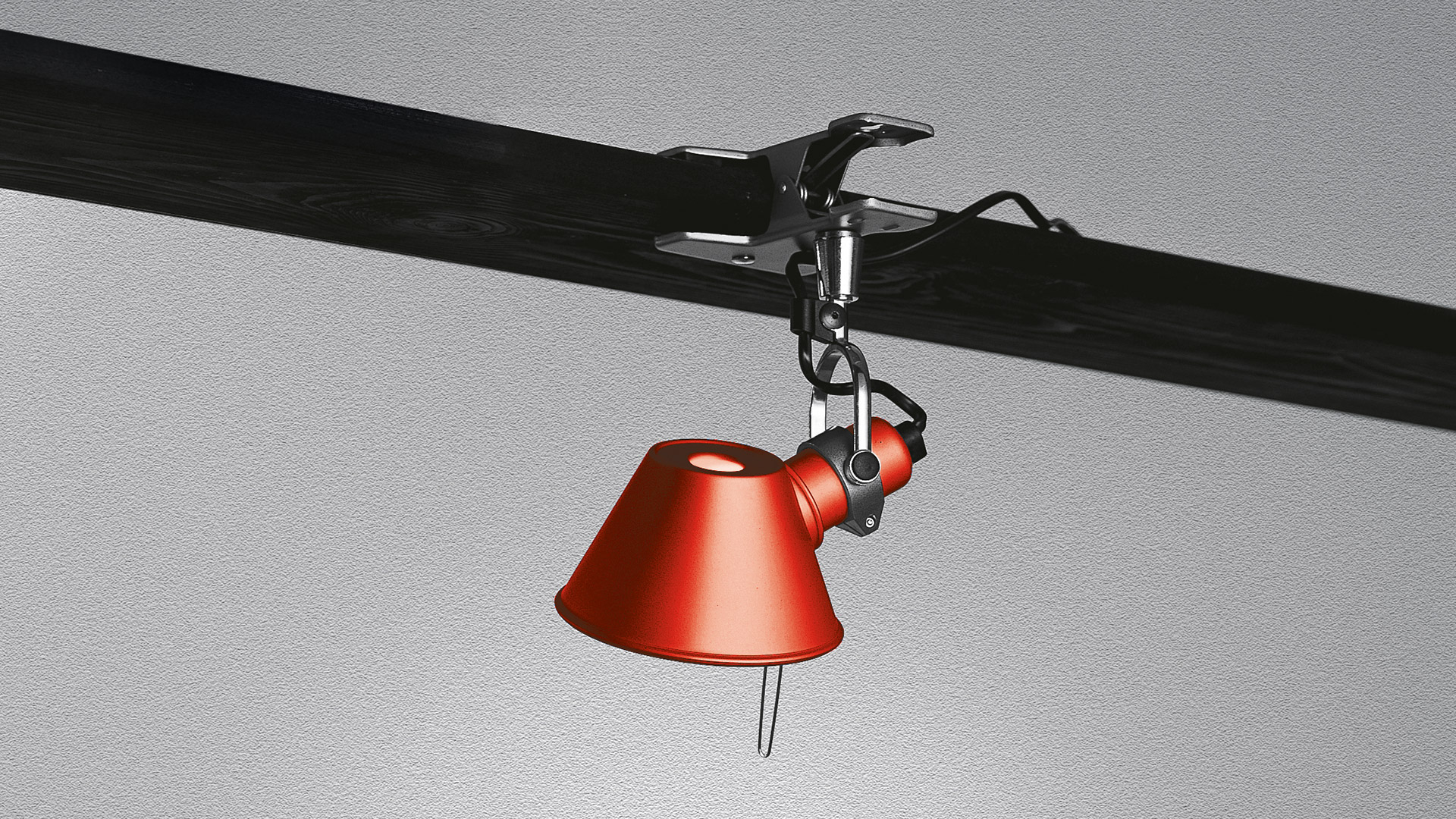 Artemide Tolomeo Pinza clip lamp in red, clamped to a dark beam, with adjustable arm and conical shade pointing downward