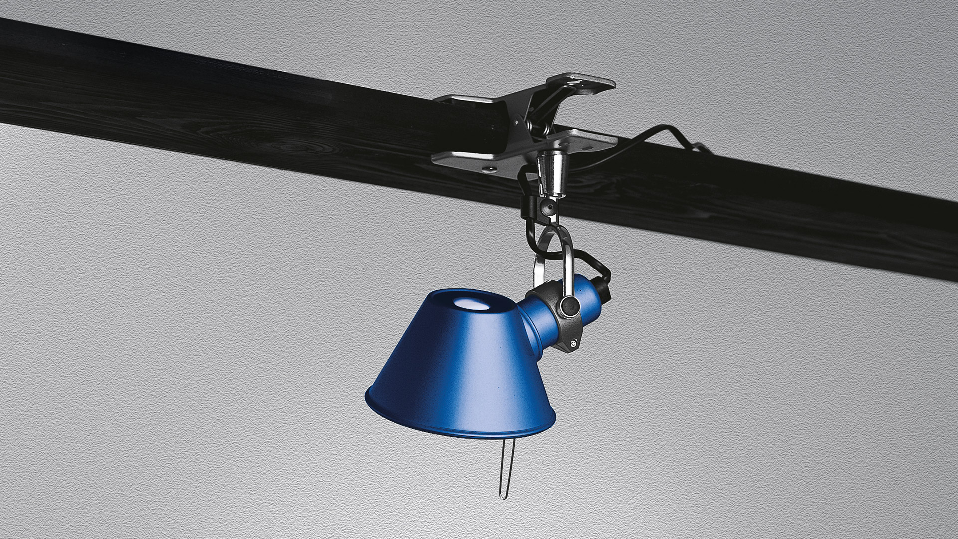 Artemide Tolomeo Pinza clip lamp in blue, clamped to a dark beam, featuring a conical shade hanging downward