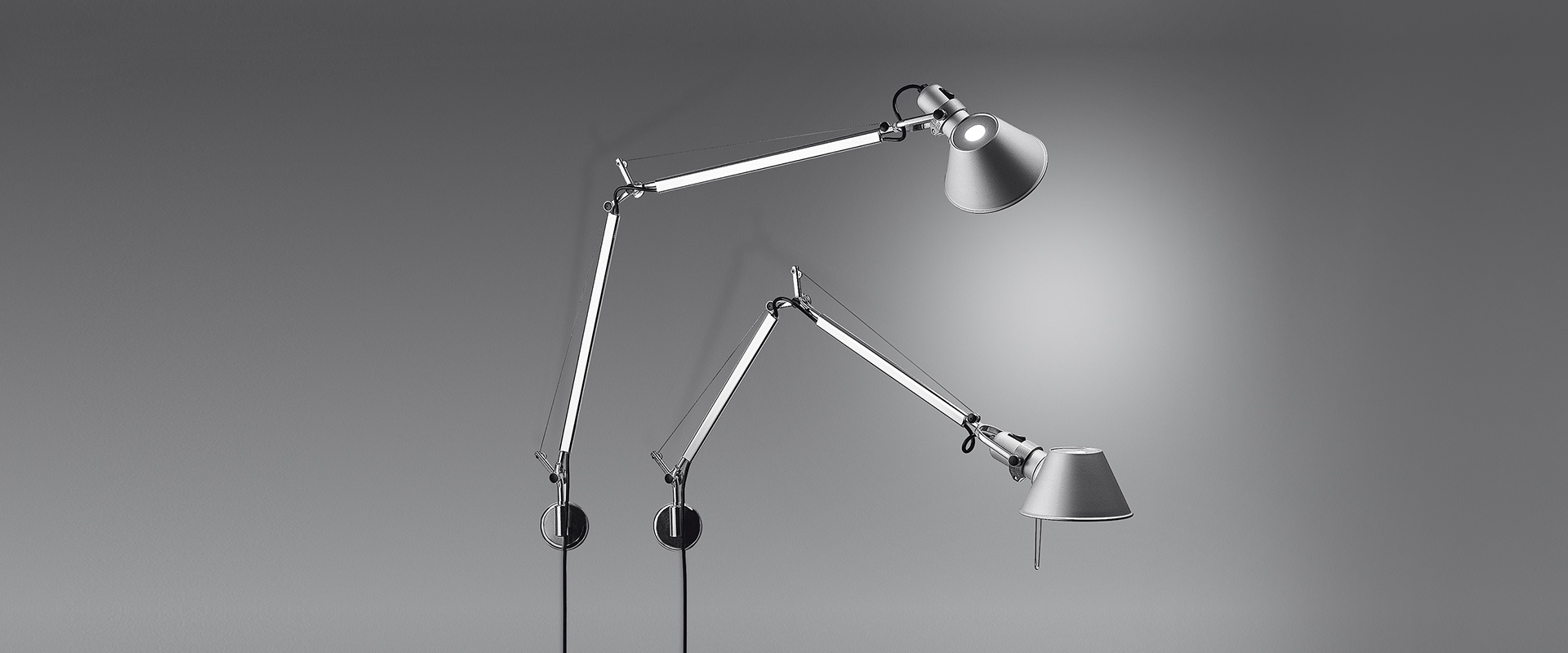 Two Artemide Tolomeo Parete wall lamps in aluminum, featuring articulated arms and adjustable shades, mounted on a grey background