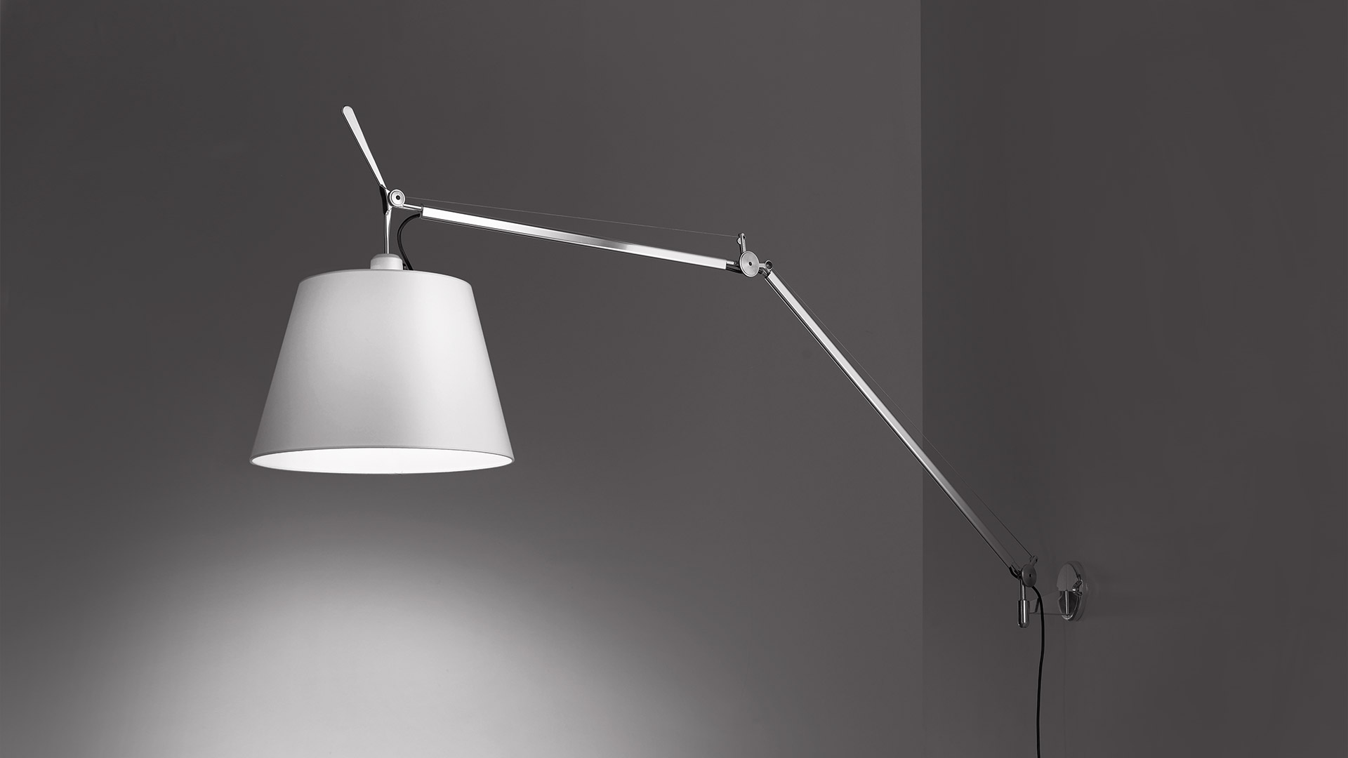 Artemide Tolomeo Mega Parete wall lamp with adjustable aluminum arm and large white conical shade, mounted on grey wall