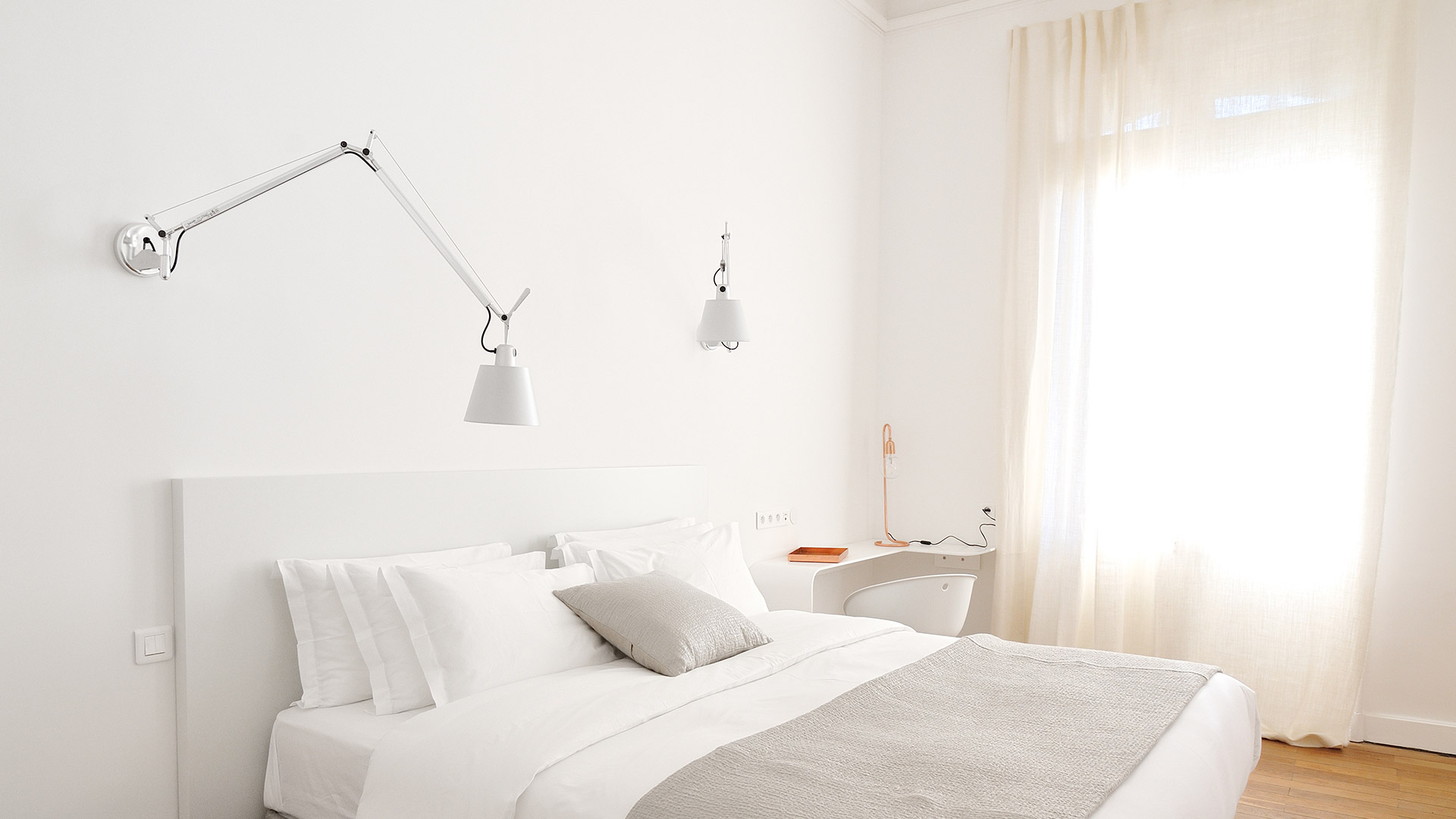 Minimalist white bedroom with two Artemide Tolomeo wall lamps flanking a bed with white linens and a mustard yellow throw.
