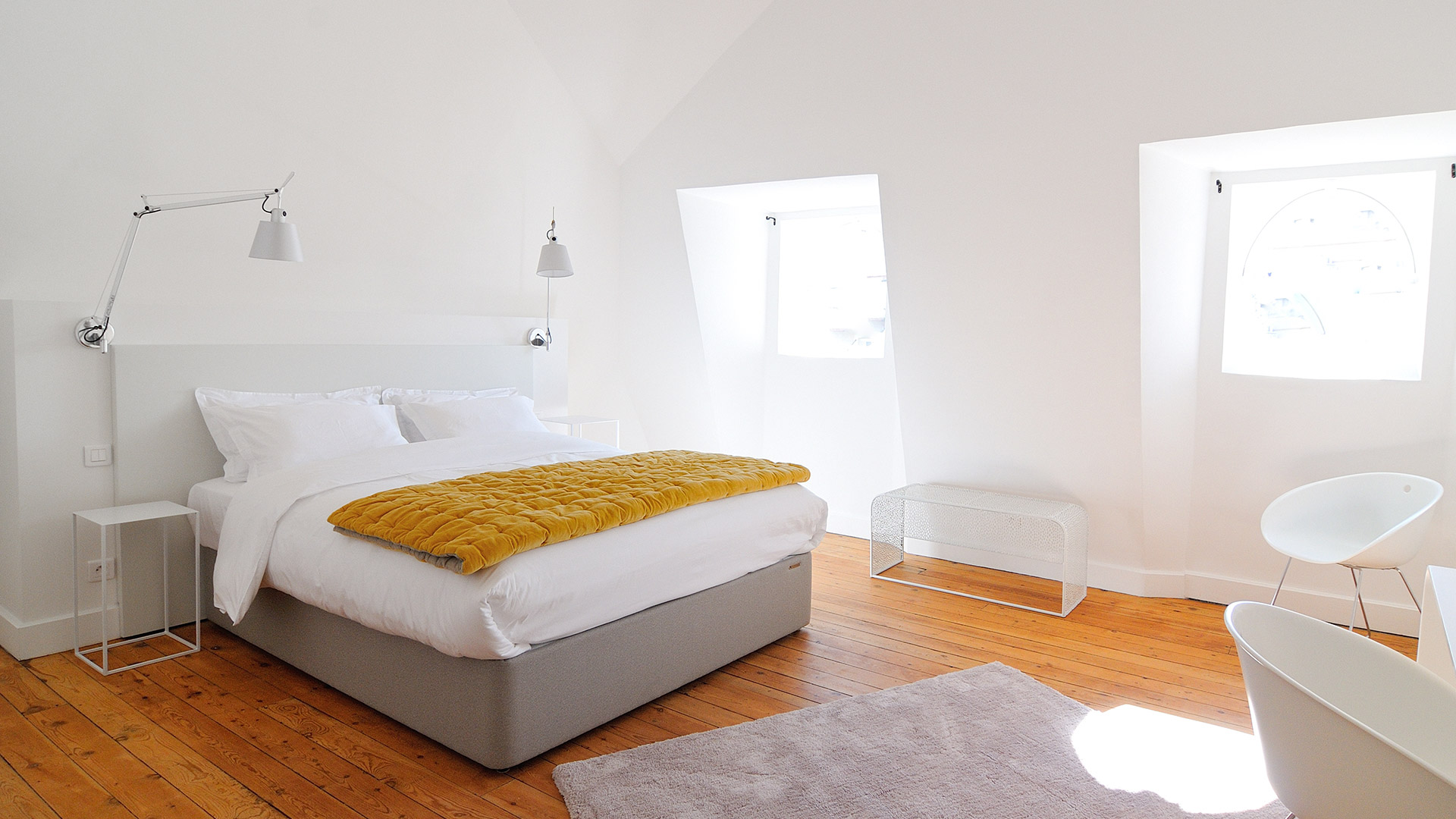 Minimalist white bedroom with two Artemide Tolomeo wall lamps mounted above a bed, providing adjustable reading light.