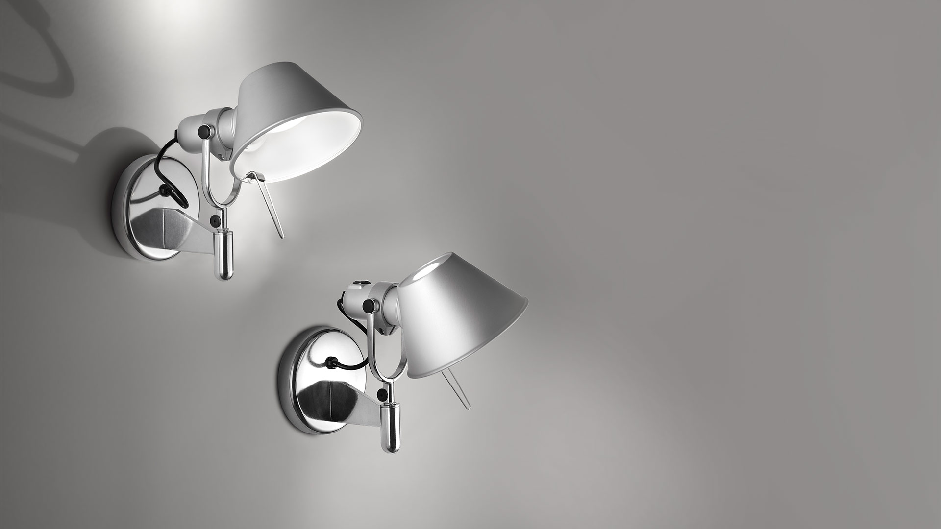 Two Artemide Tolomeo wall lamps in aluminum with adjustable arms and conical shades mounted on chrome wall brackets.