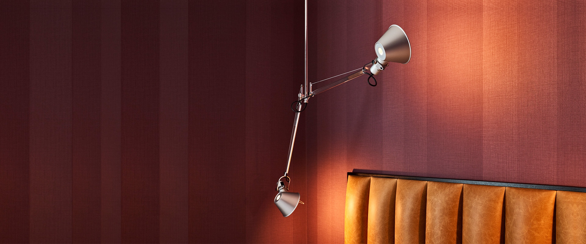 Tolomeo Due Bracci Sospensione: two adjustable aluminum pendant lamps with articulated arms, mounted on wall above orange leather sofa