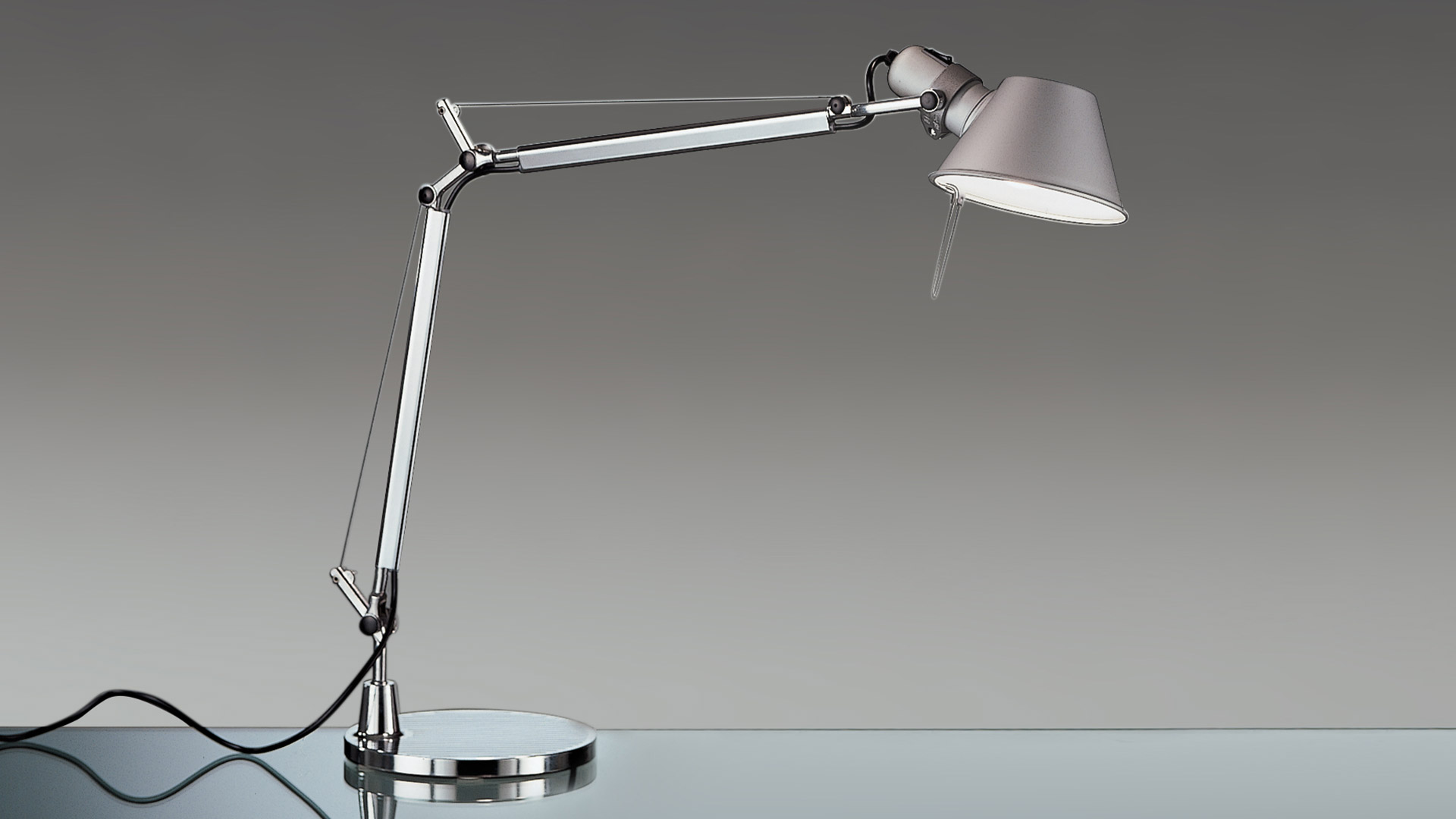 Artemide Tolomeo Mini Tavolo desk lamp with circular aluminum reflector and articulated arm, emitting warm directional light