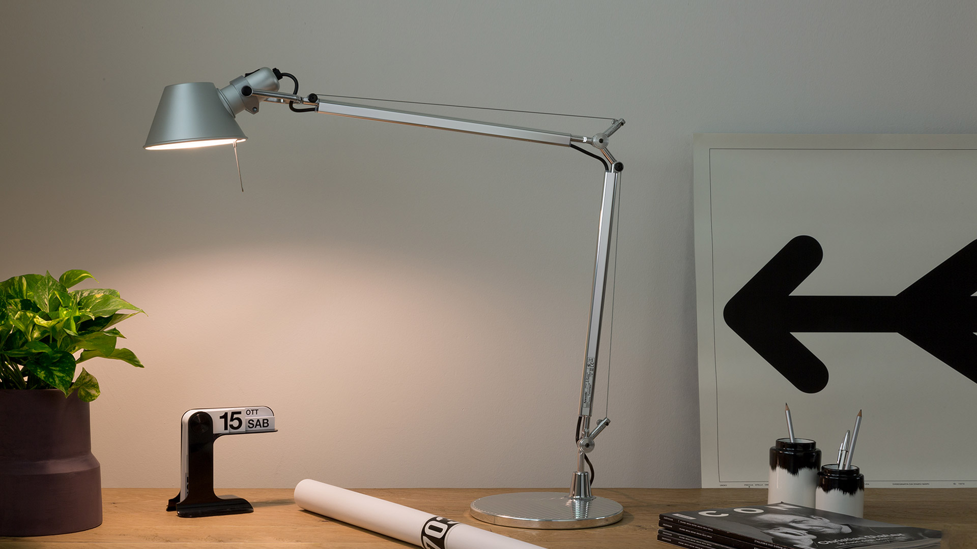 Artemide Tolomeo Tavolo desk lamp in aluminum on a white desk, featuring adjustable articulated arm and conical shade