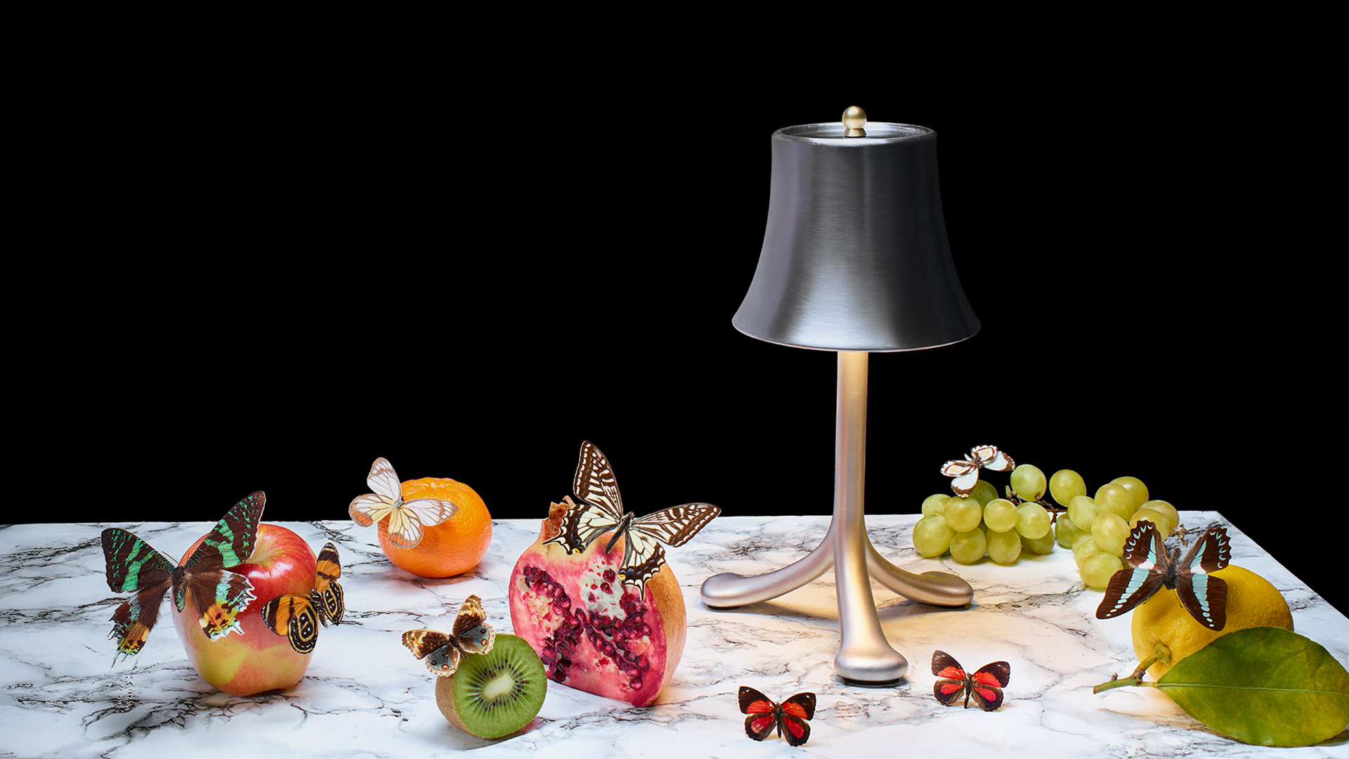 Trois Rois table lamp by Artemide: silver bell-shaped shade on three-legged base emitting warm light, with glasses beside it
