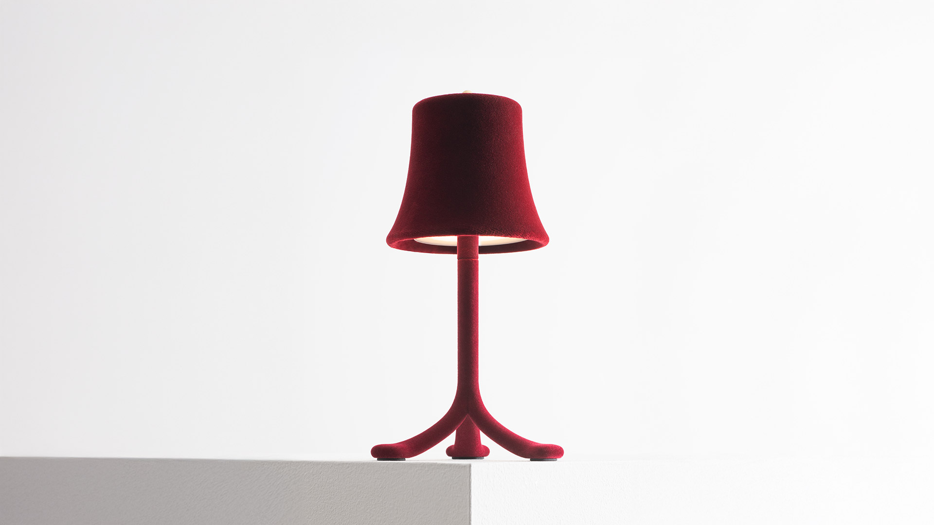 Close-up of Artemide Trois Rois table lamp with deep red velvet bell-shaped shade and matching stem, glowing LED base