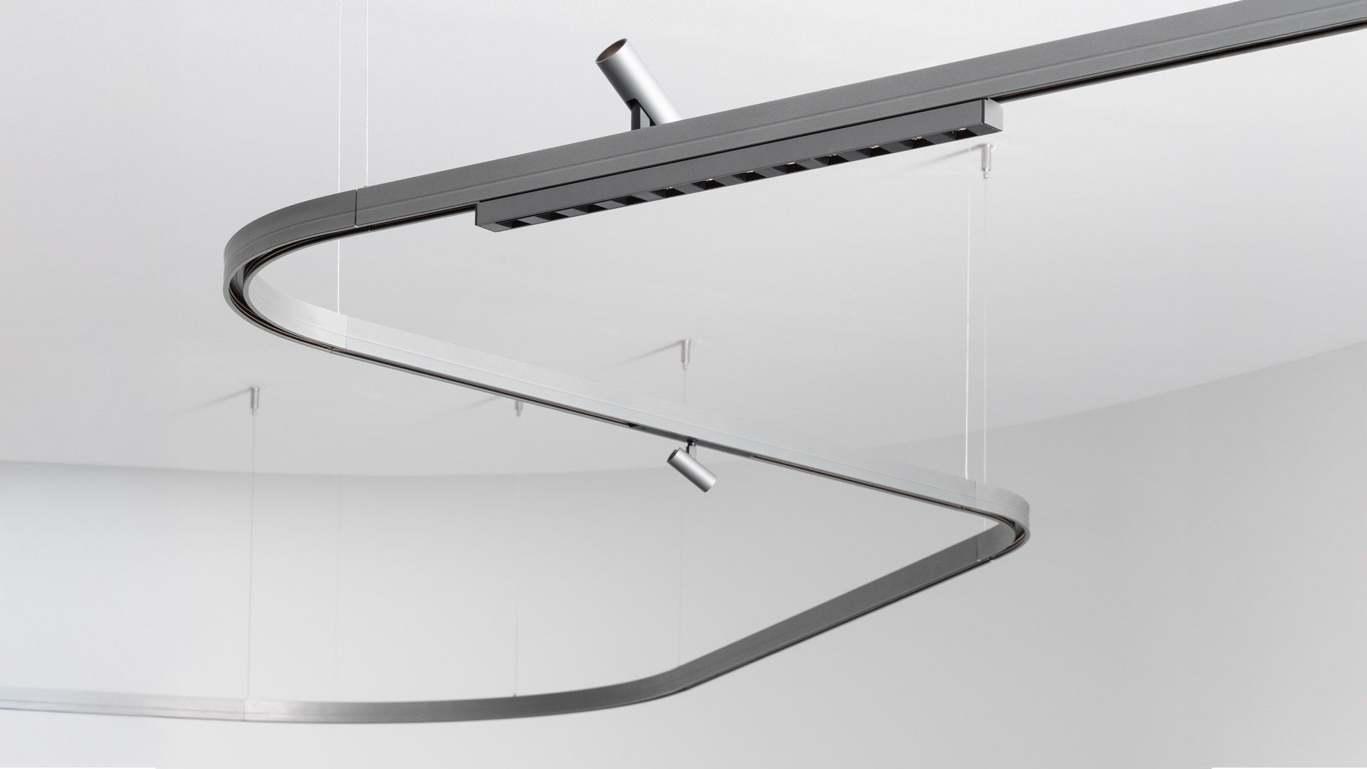 Artemide Turn Around System: dark grey tubular loop pendant light intersecting a linear track rail, featuring two downlight nozzles