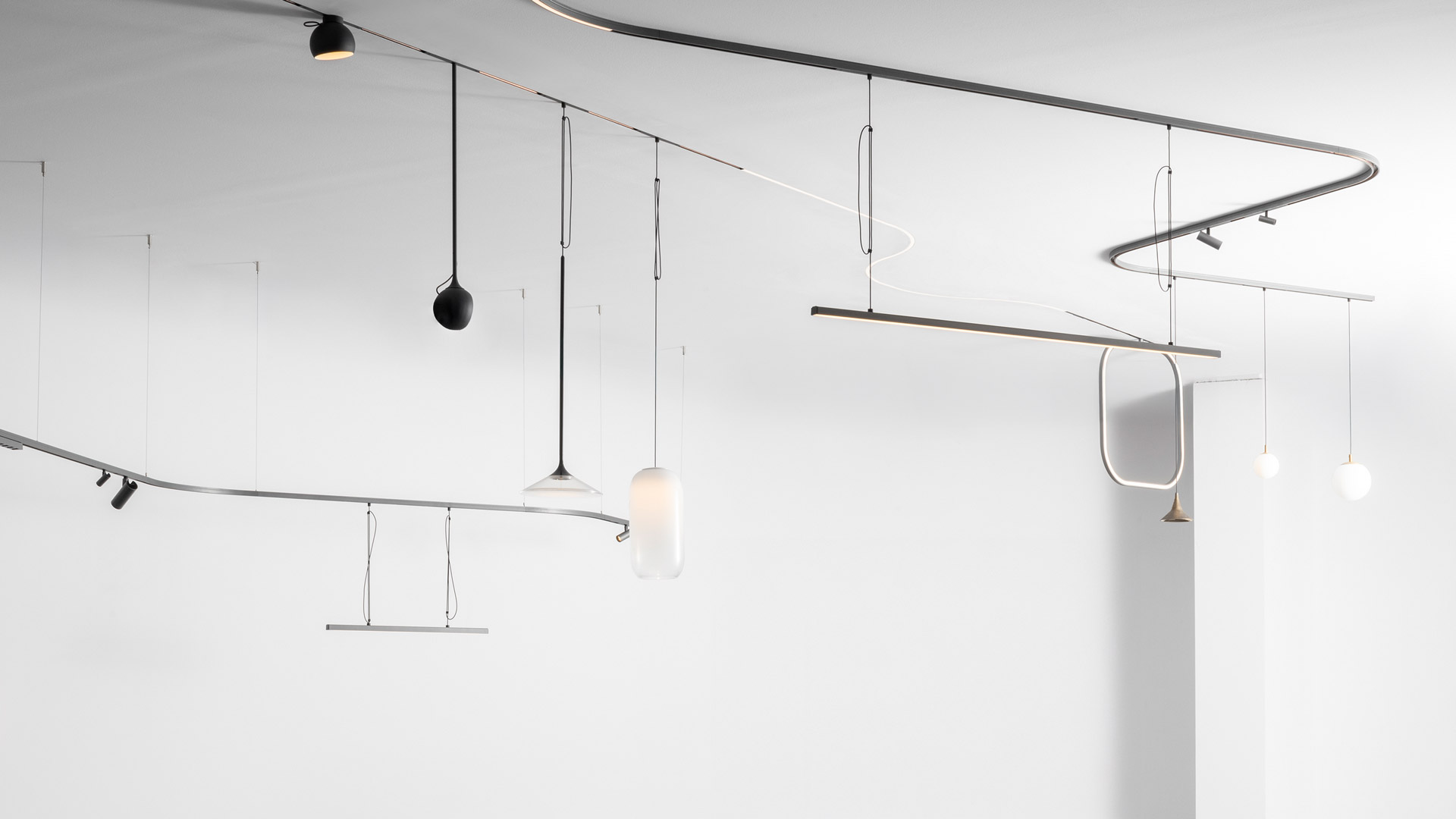 Artemide Turn Around System: black ceiling track with spotlights, pendant lights with glass diffusers, and a large circular wall lamp