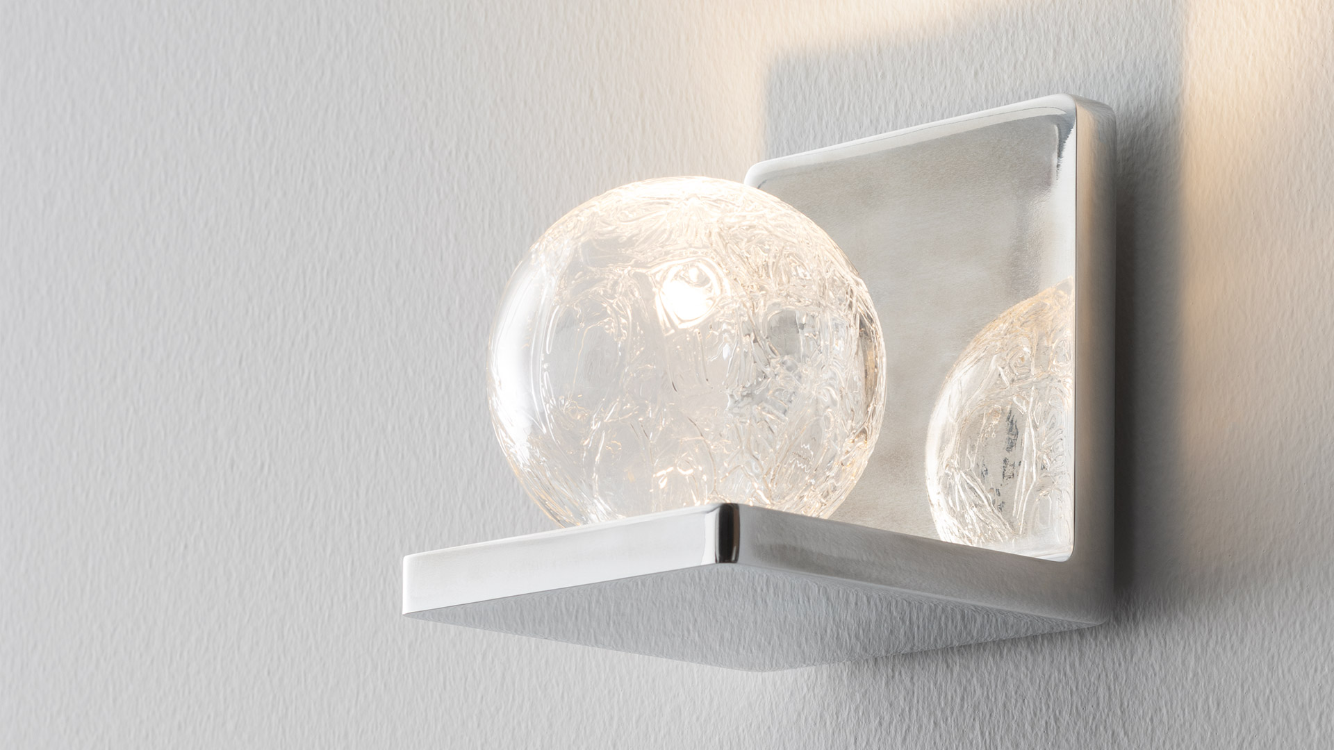 Two Artemide Ulrich und Diotima wall sconces: left in silver aluminum, right in brown finish, both emitting warm upward light.