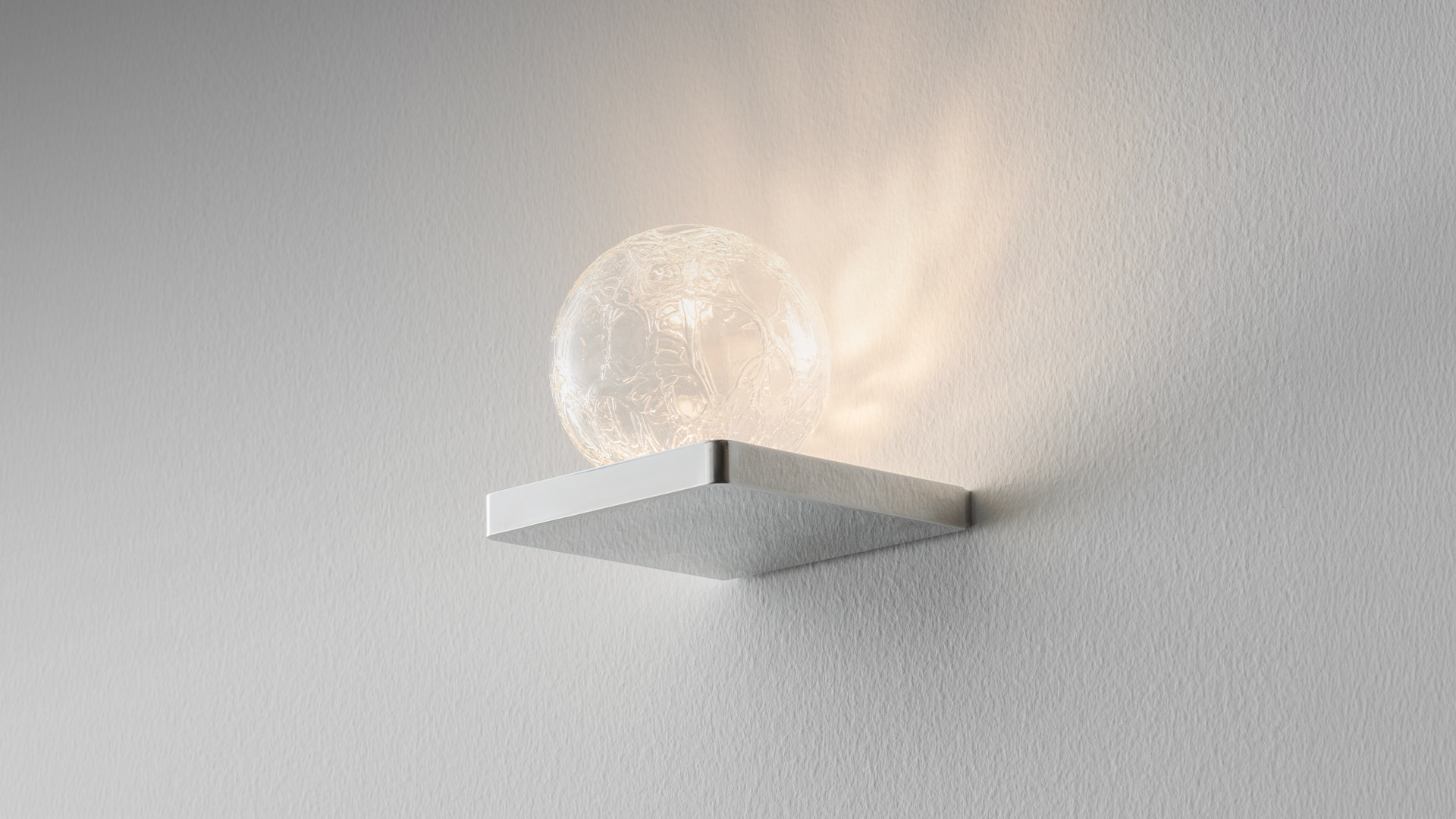 Close-up of a spherical transparent glass diffuser with intricate organic relief texture, creating a sculptural light-diffusing surface