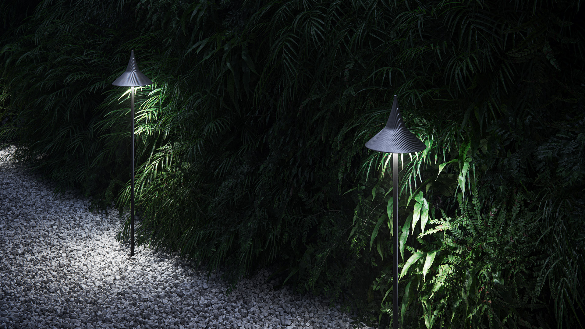 Two Artemide Unterlinden Outdoor bollard lamps with dark conical shades illuminating a gravel garden path bordered by lush greenery at night