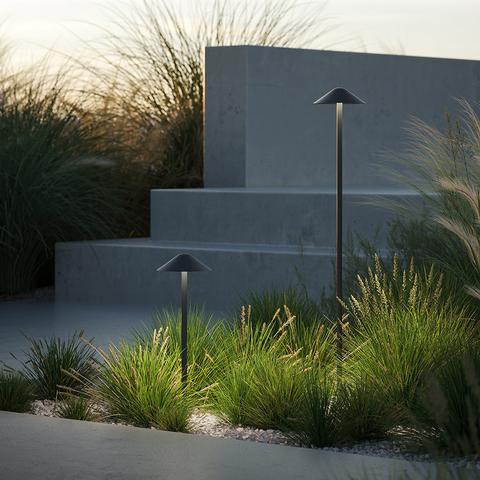 Two Artemide Vea Bollard outdoor path lights with conical dark shades on slender poles, illuminating a modern garden at dusk