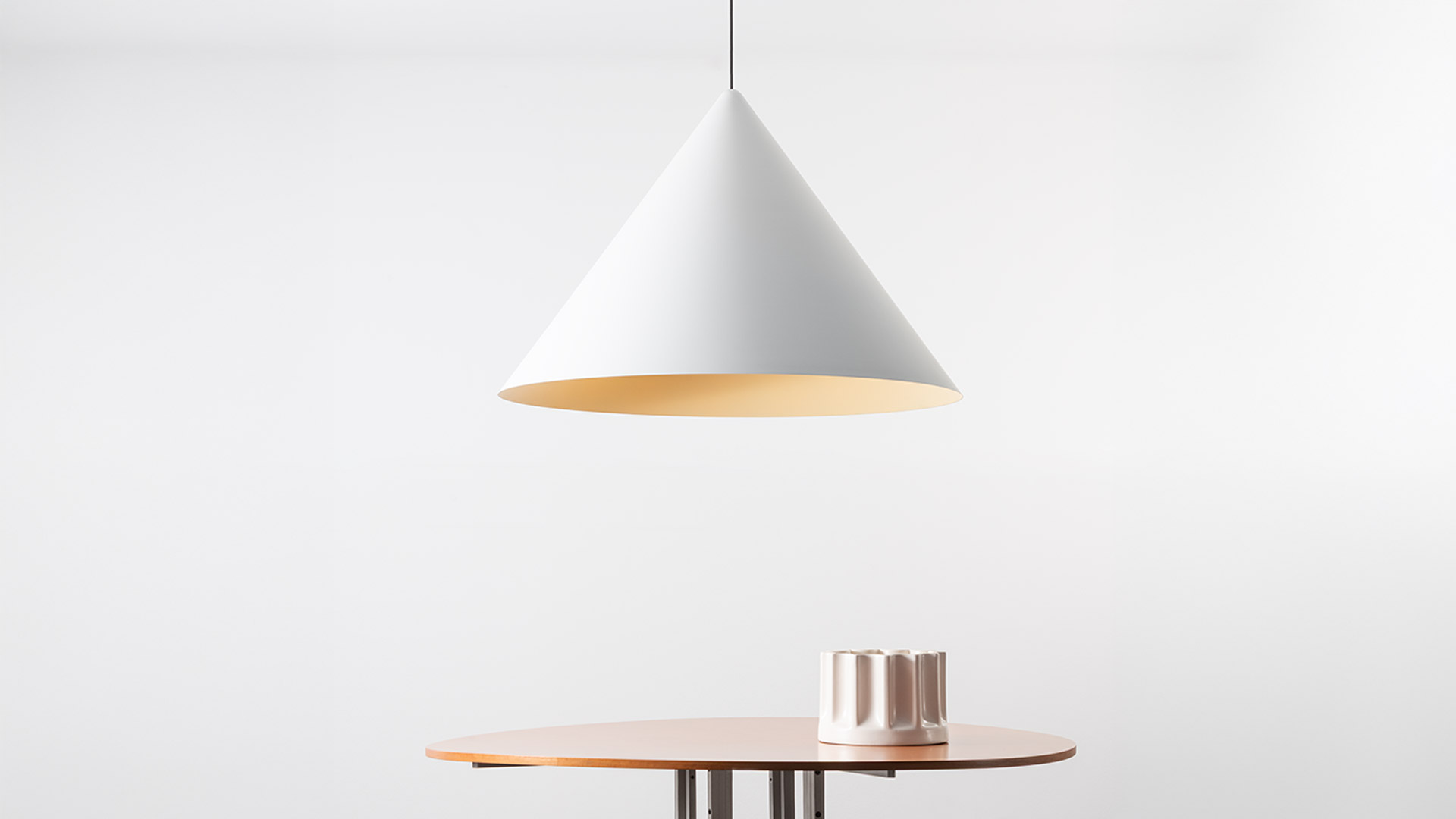 Artemide Vea Suspension pendant lamp with white conical shade and warm gold interior, hanging above a round wooden table.