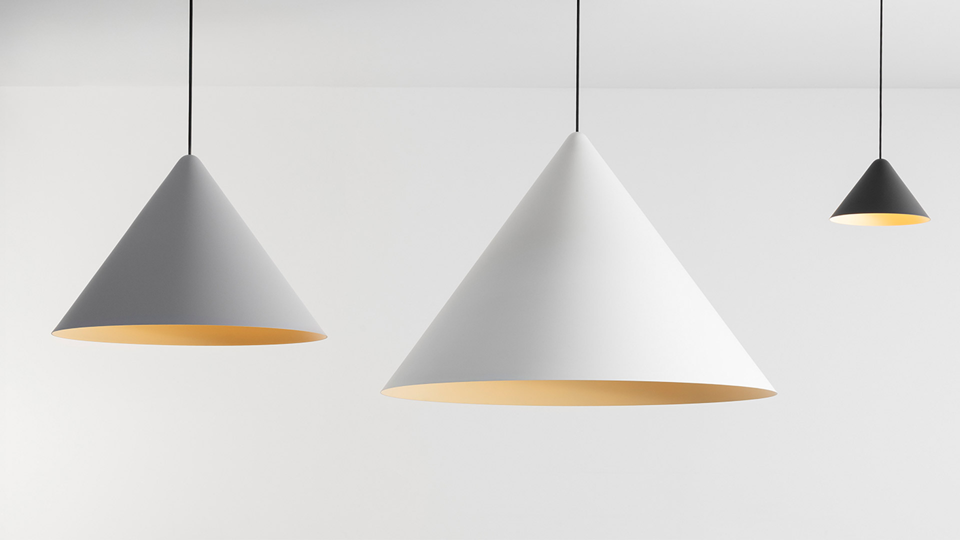 Three Artemide Vea pendant lamps in gray, white, and black conical shades with warm golden interiors, suspended on black cords