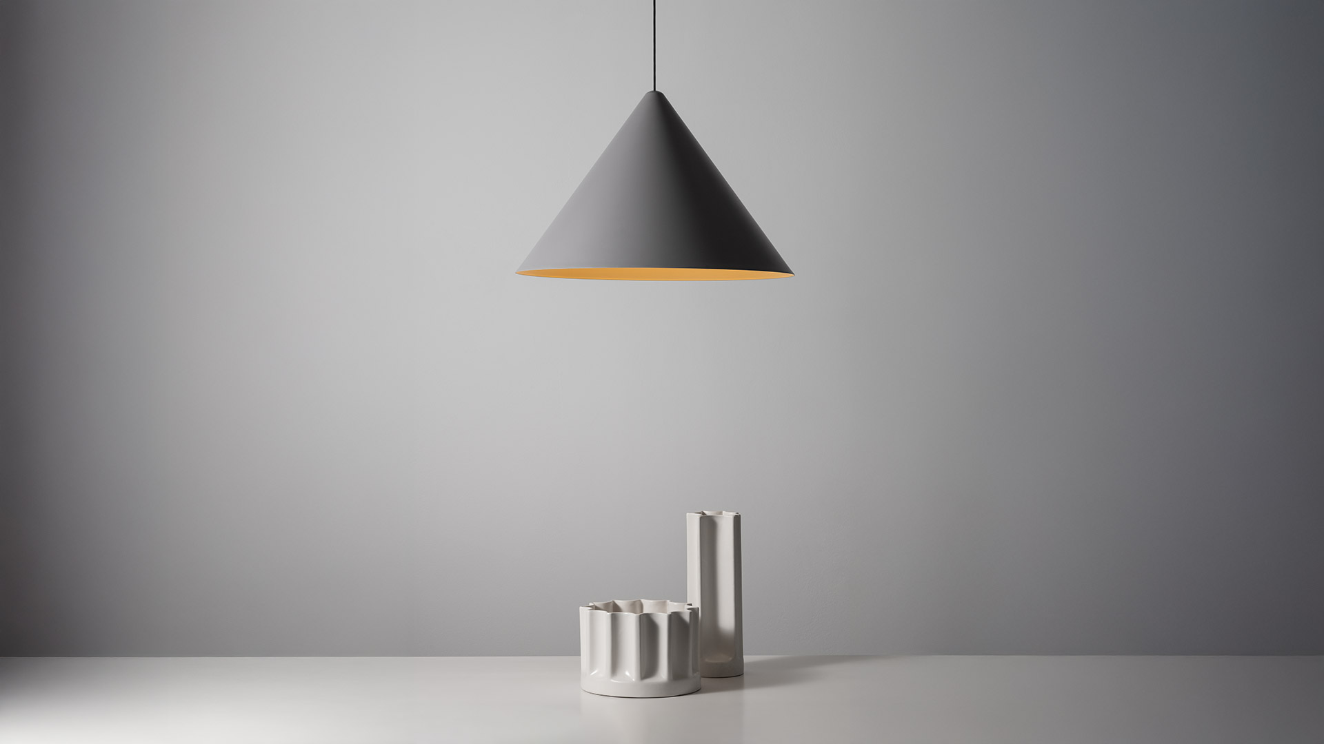 Artemide Vea Suspension: woman touching flat disc underside showing gold interior, paired with conical white pendant lamp with warm gold inner shade