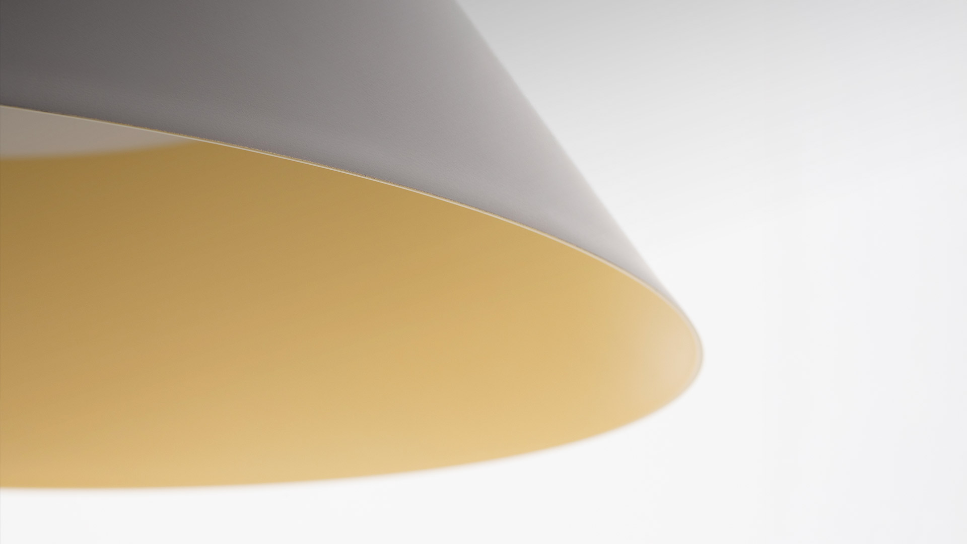Vea pendant lamp by Artemide: dark grey conical shade with warm gold interior, suspended above white sculptural decorative objects on a surface