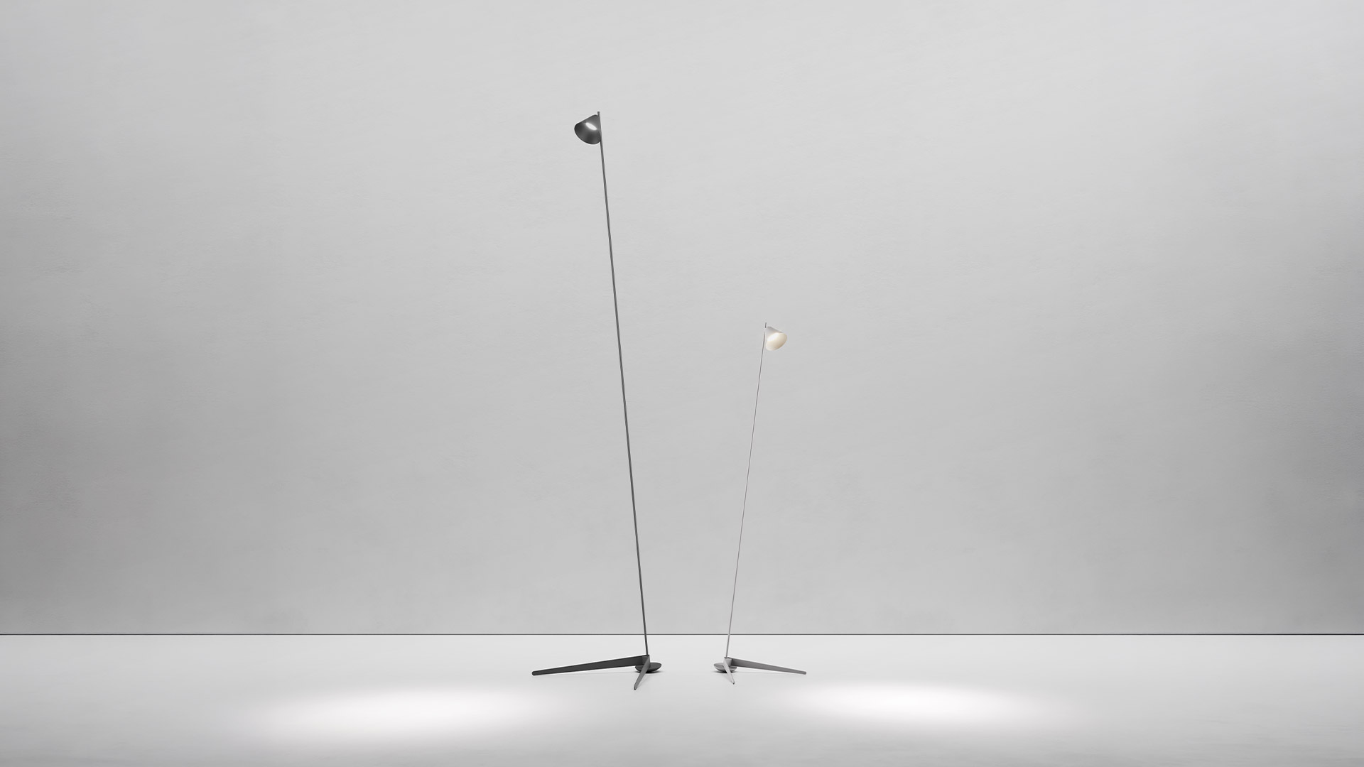 Two Artemide Vea floor lamps with slim black arms and conical shades on tripod bases, casting focused light pools on the floor