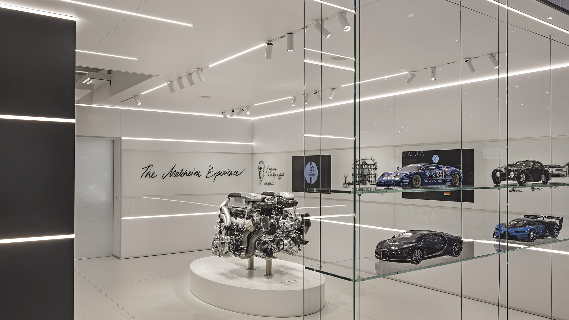 Artemide Vector and Vector Magnetic linear LED lights illuminate a sleek automotive showroom displaying a Bugatti engine and scale car models