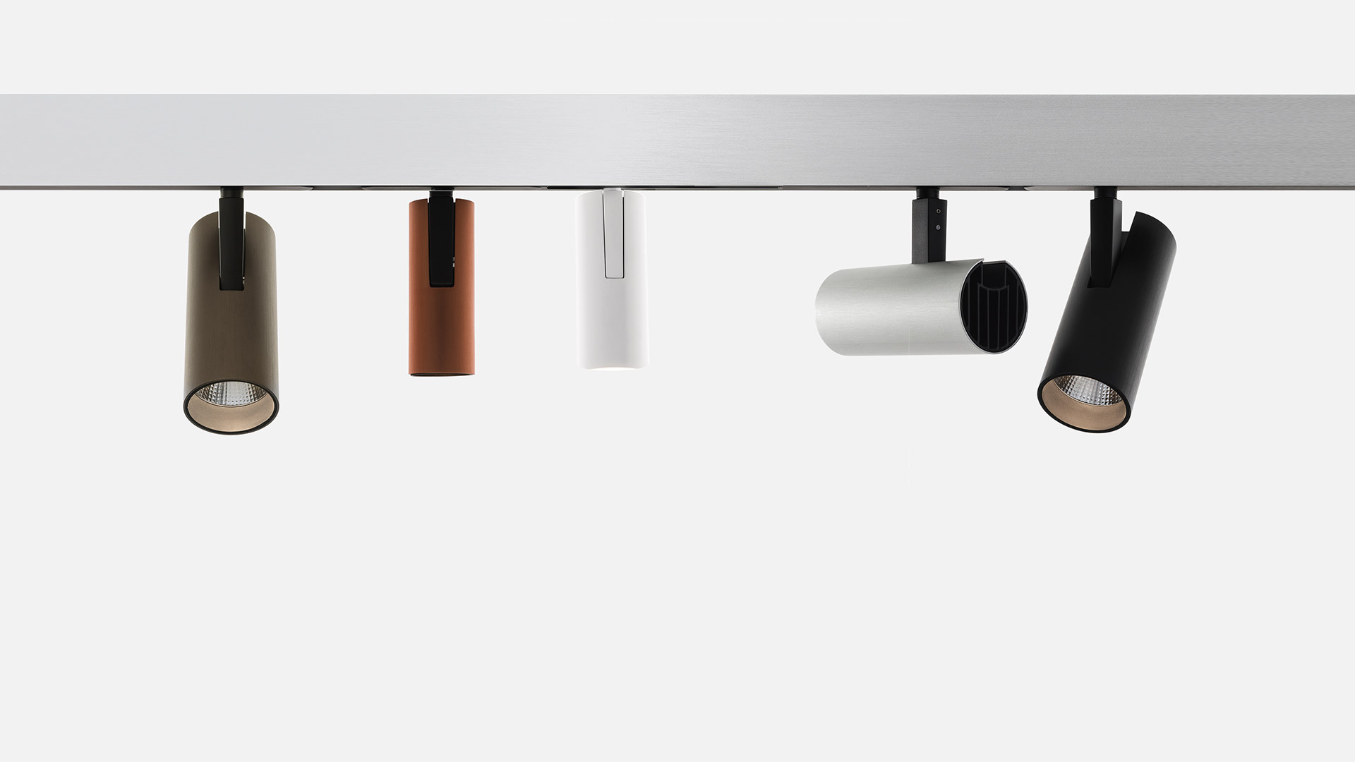 Five Artemide Vector track spotlights in olive, copper, white, light grey, and black cylindrical housings mounted on a magnetic rail