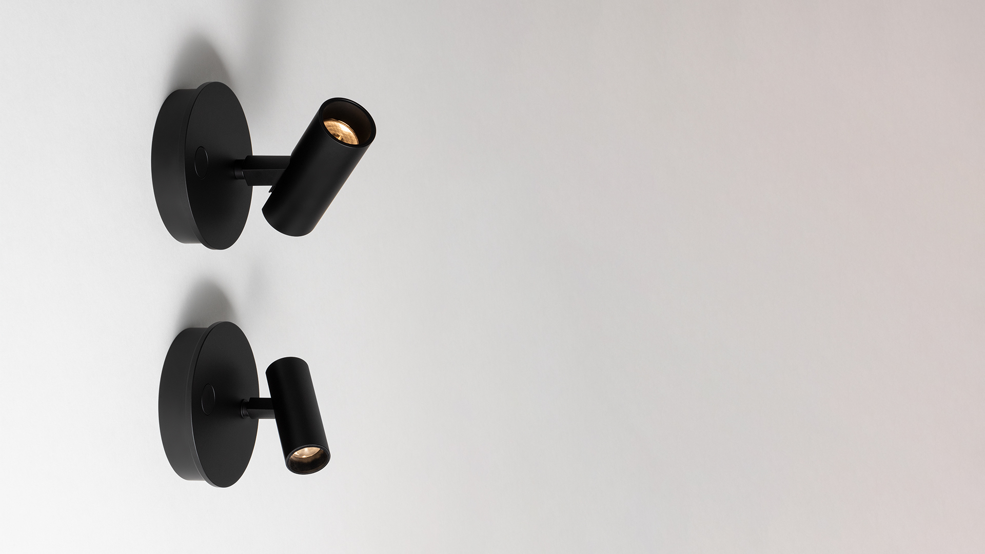 Two Artemide Vector Wall spotlights in matte black, mounted on round bases, with adjustable cylindrical heads directing warm LED light.