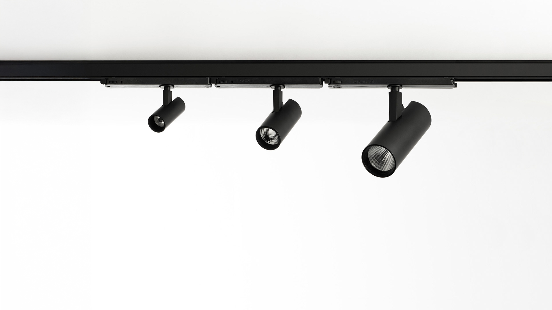 Artemide Vector Track 230V black cylindrical spotlight mounted on ceiling track, projecting a vivid purple light beam on wall