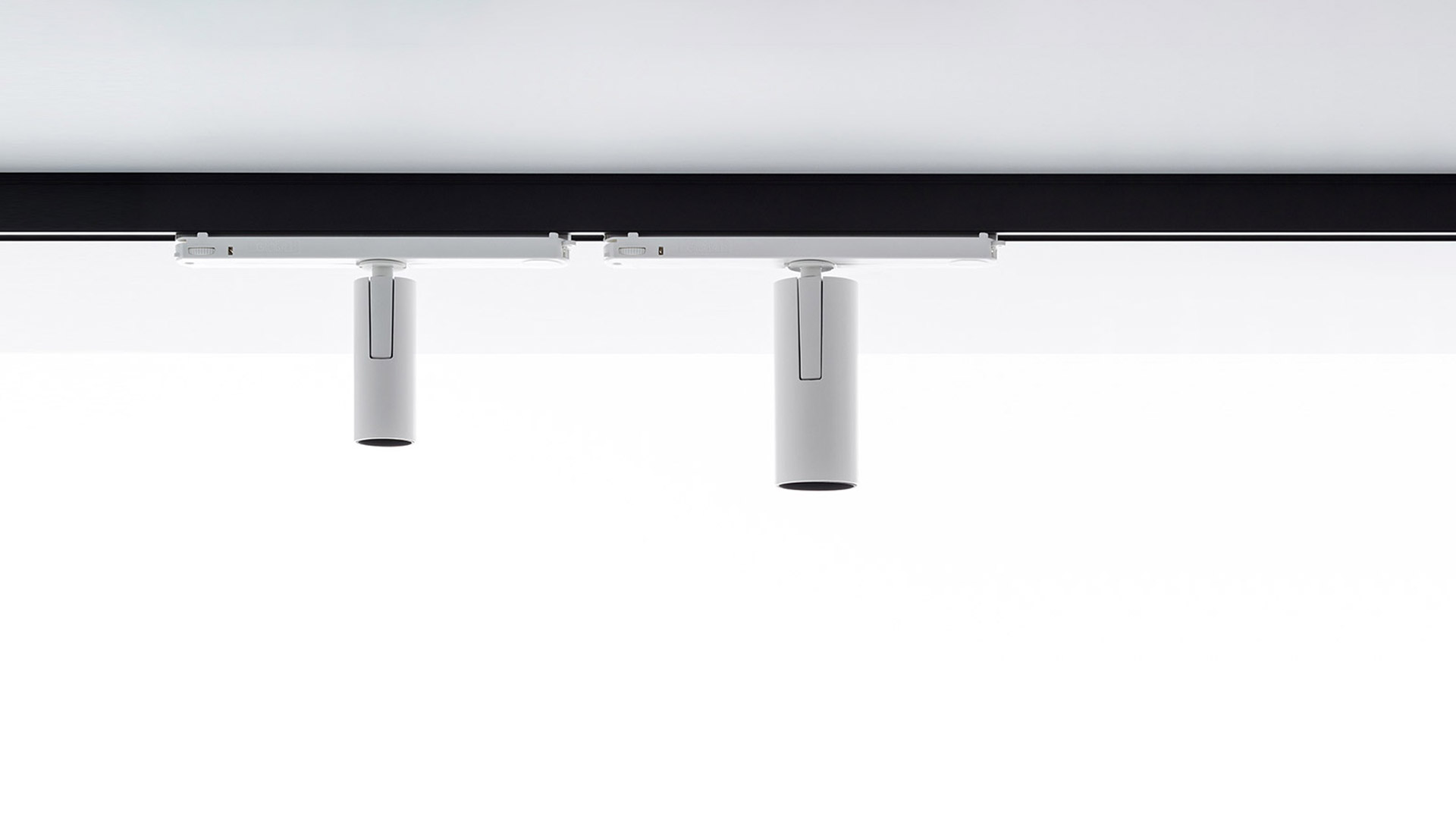 Two white cylindrical Artemide Vector Track 230V spotlights mounted on a black ceiling track rail, directed downward.