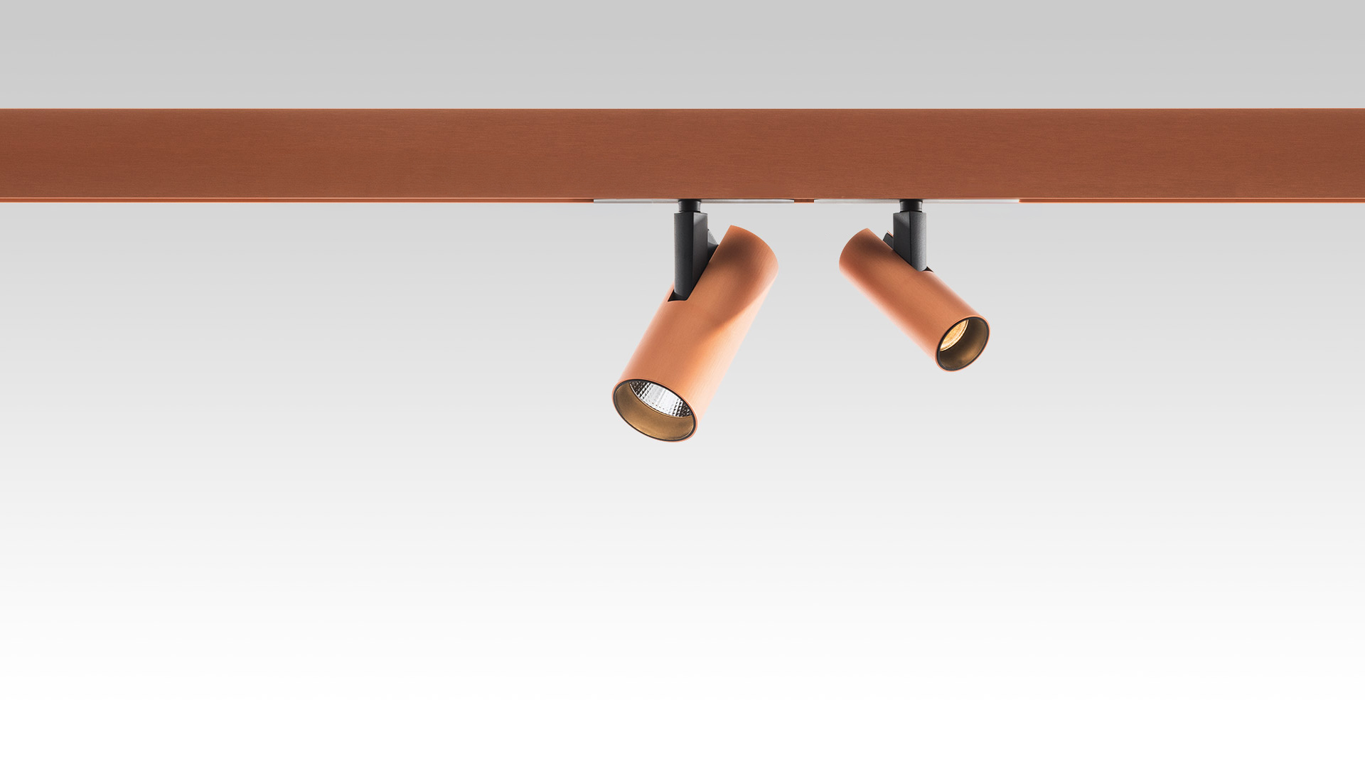 Two adjustable terracotta-colored cylindrical LED spotlights mounted on a matching magnetic track system, angled in different directions