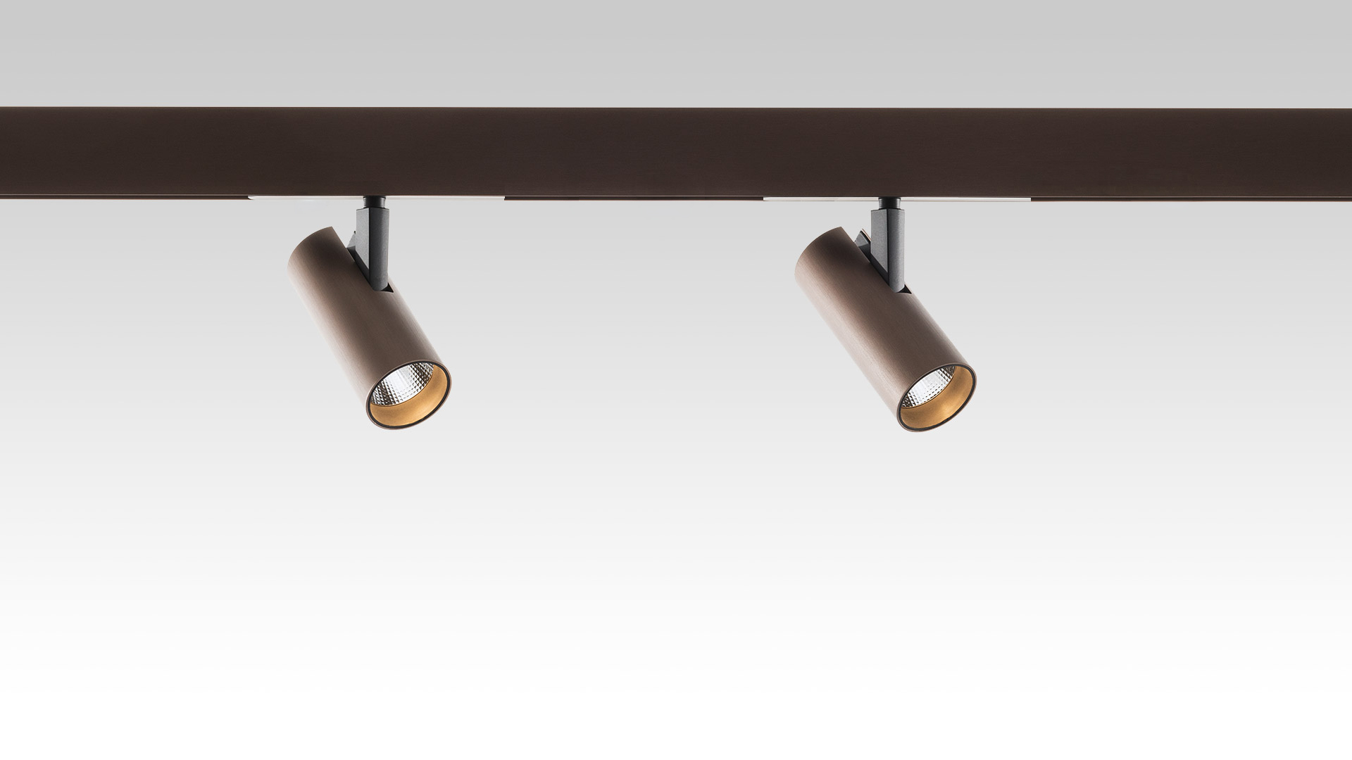 Two Artemide Vector Magnetic bronze cylindrical spotlights mounted on a dark magnetic track, heads tilted at different angles