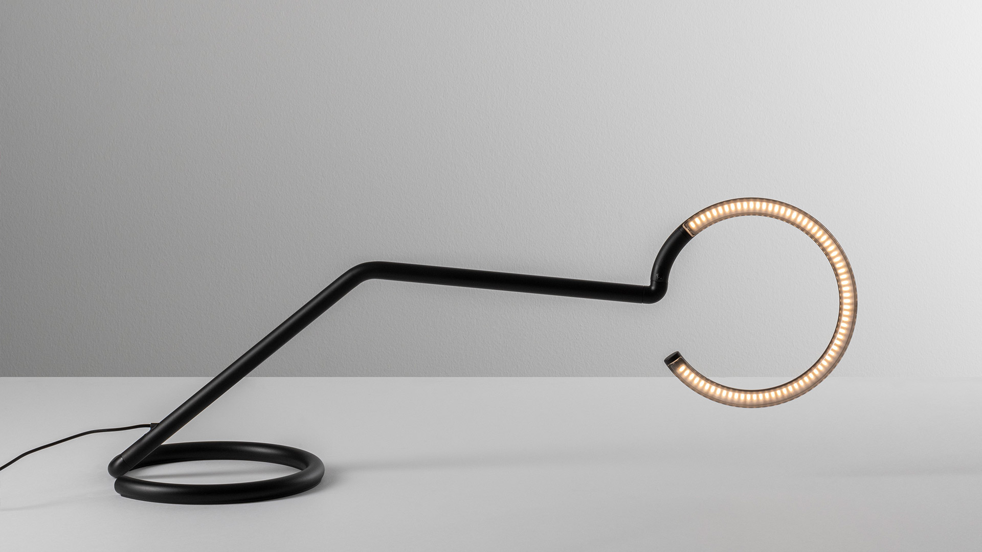 Artemide Vine Light lamps with circular LED rings on slender black arms arranged over a dining table set against a vivid blue background